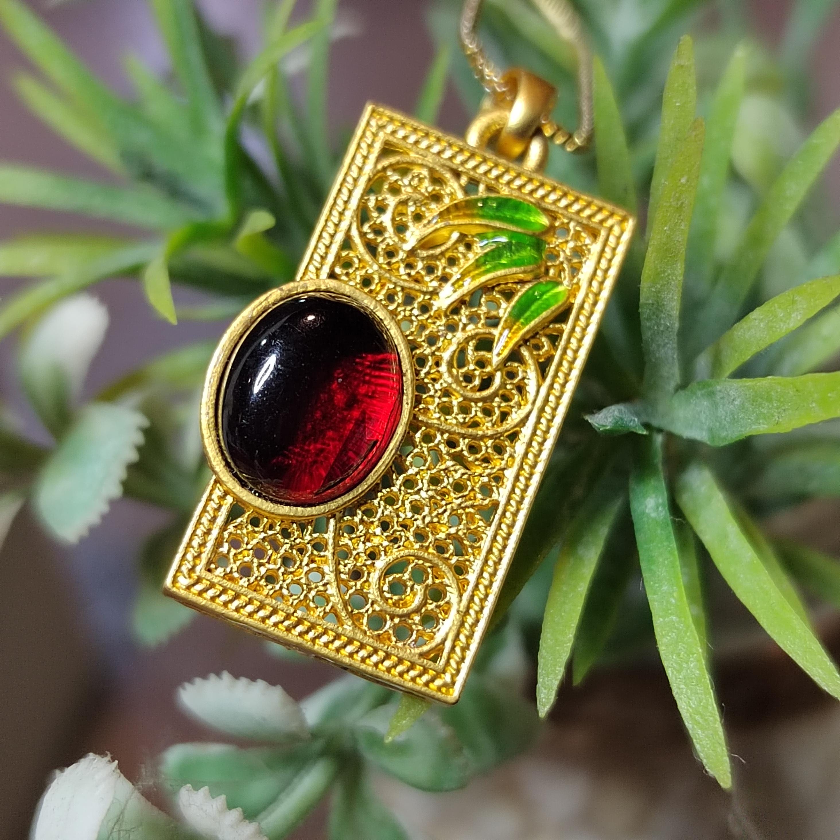 Gold pendant with red and black stone on green leaves