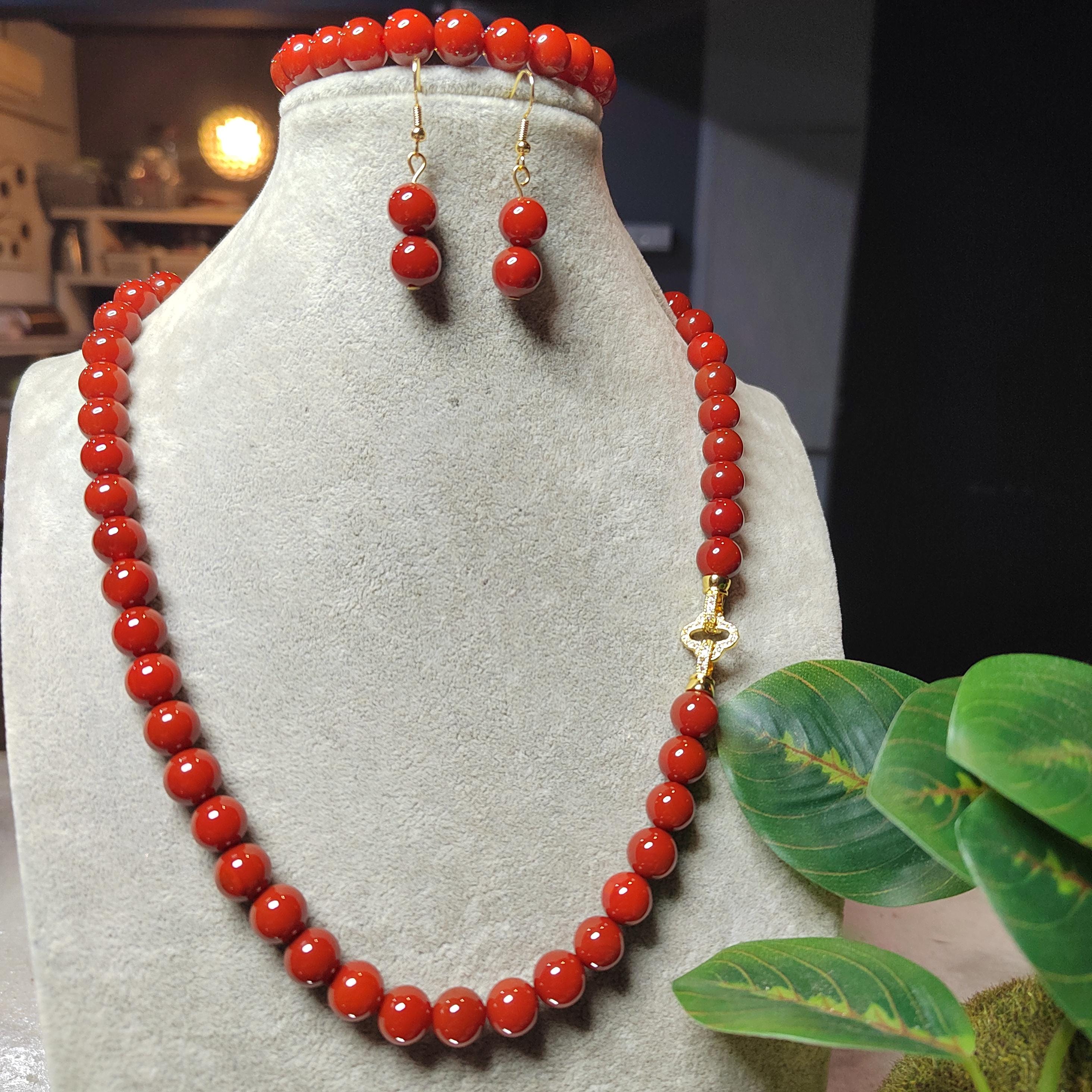 Red beaded necklace and earrings on a gray mannequin with a blurred indoor background