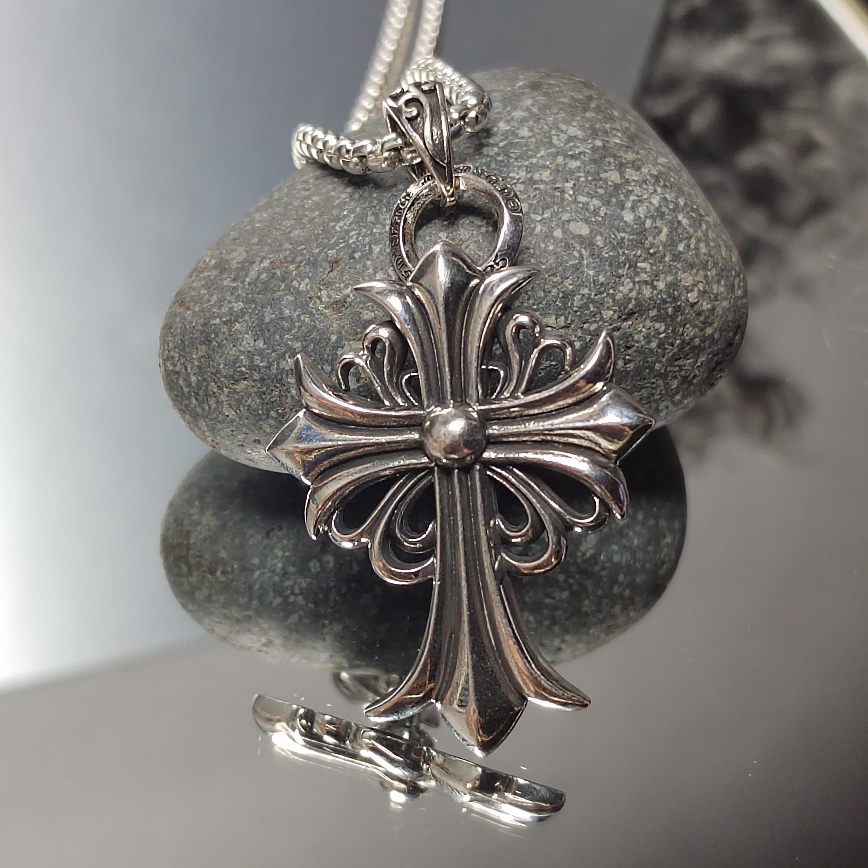 Silver cross pendant on a chain against a stone background