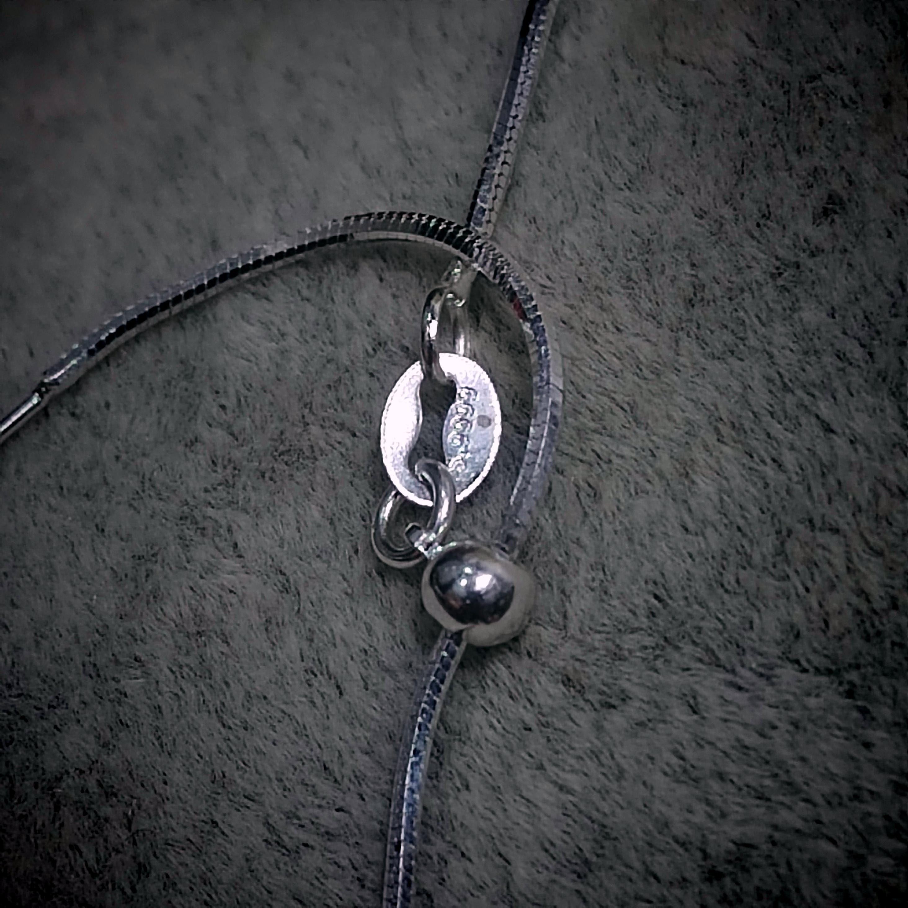 Close-up of a silver necklace with a pendant on a textured gray surface