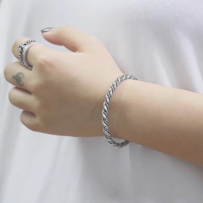 Hand wearing a silver bracelet on a plain white background