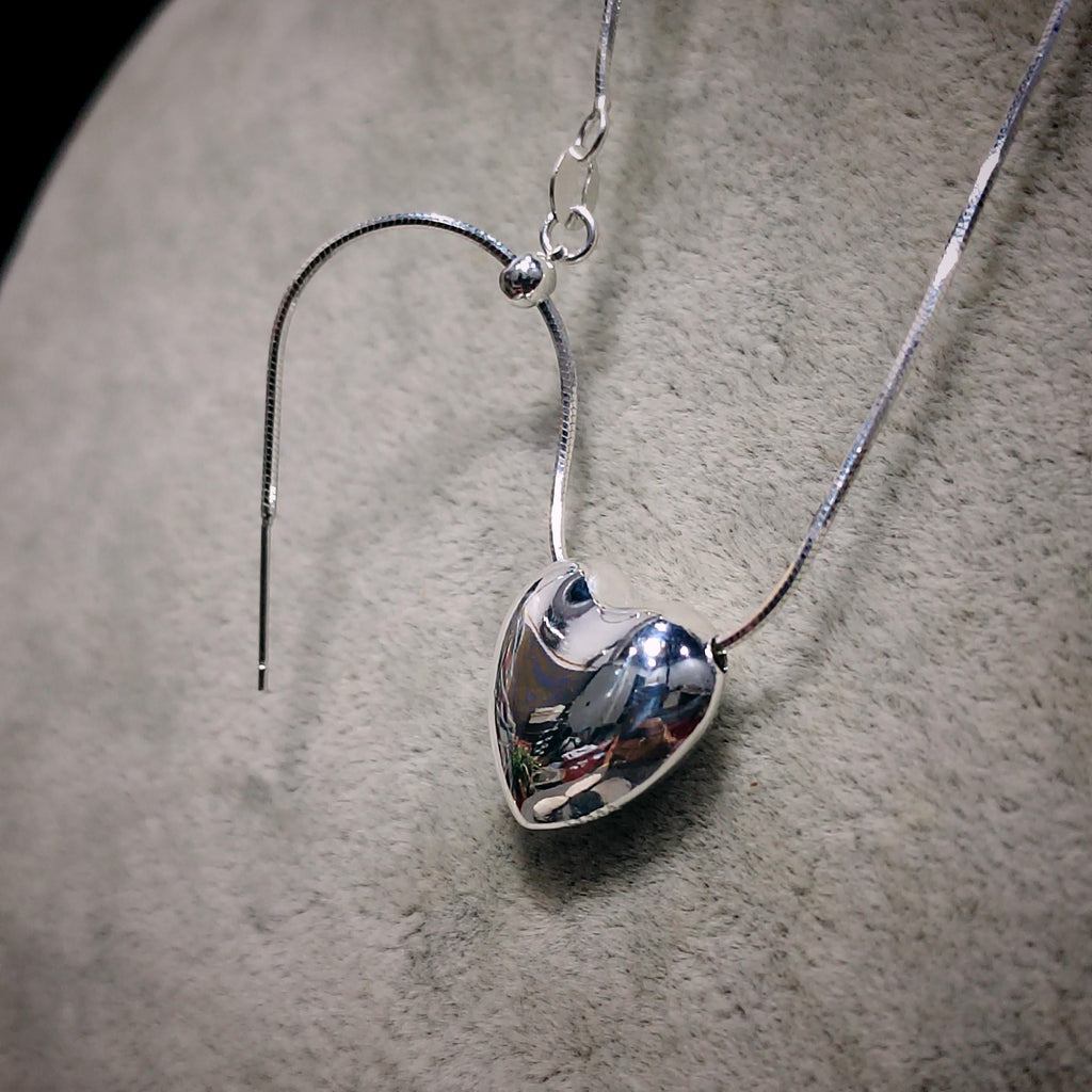Silver heart-shaped pendant on a chain against a neutral background