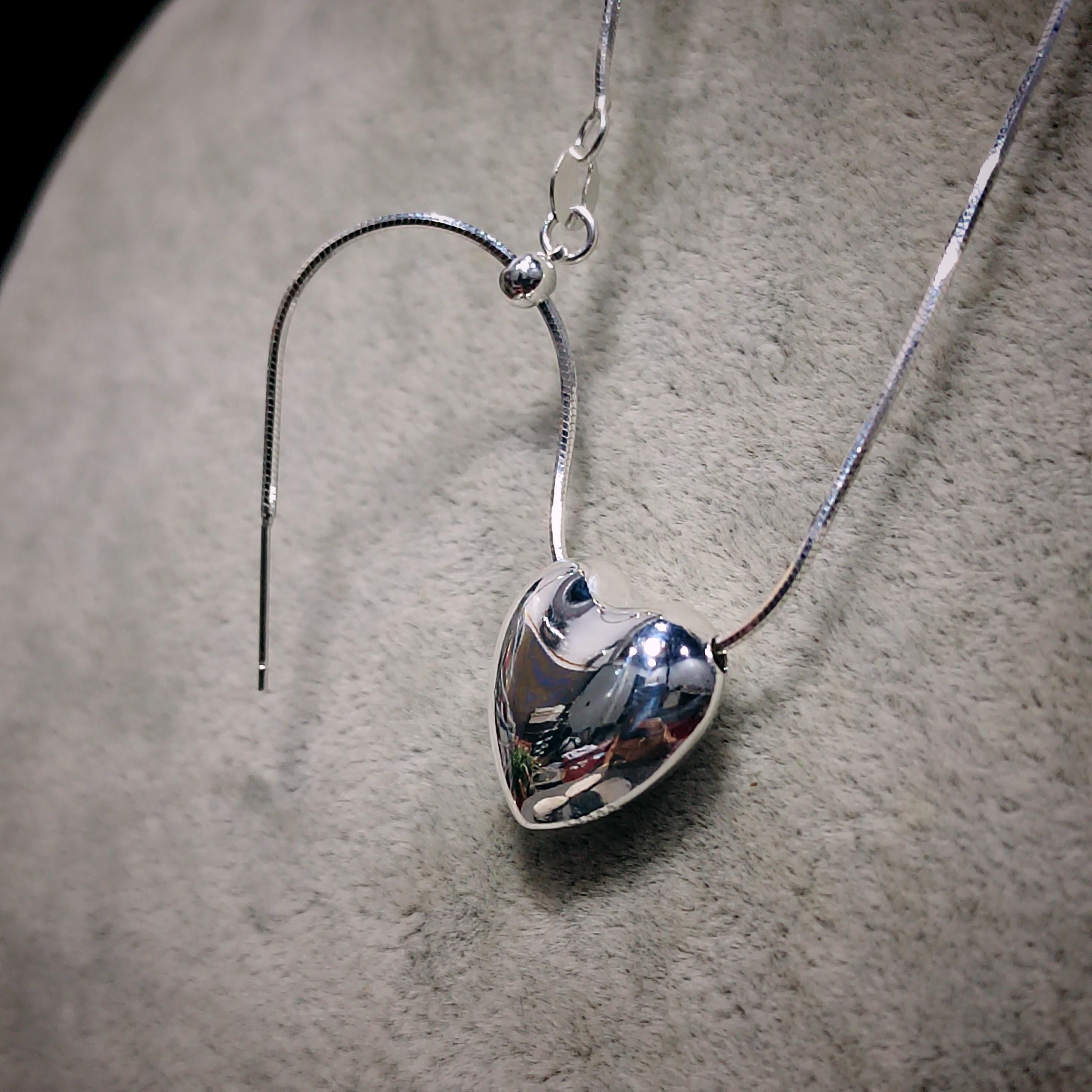 Silver heart-shaped pendant on a chain against a neutral background