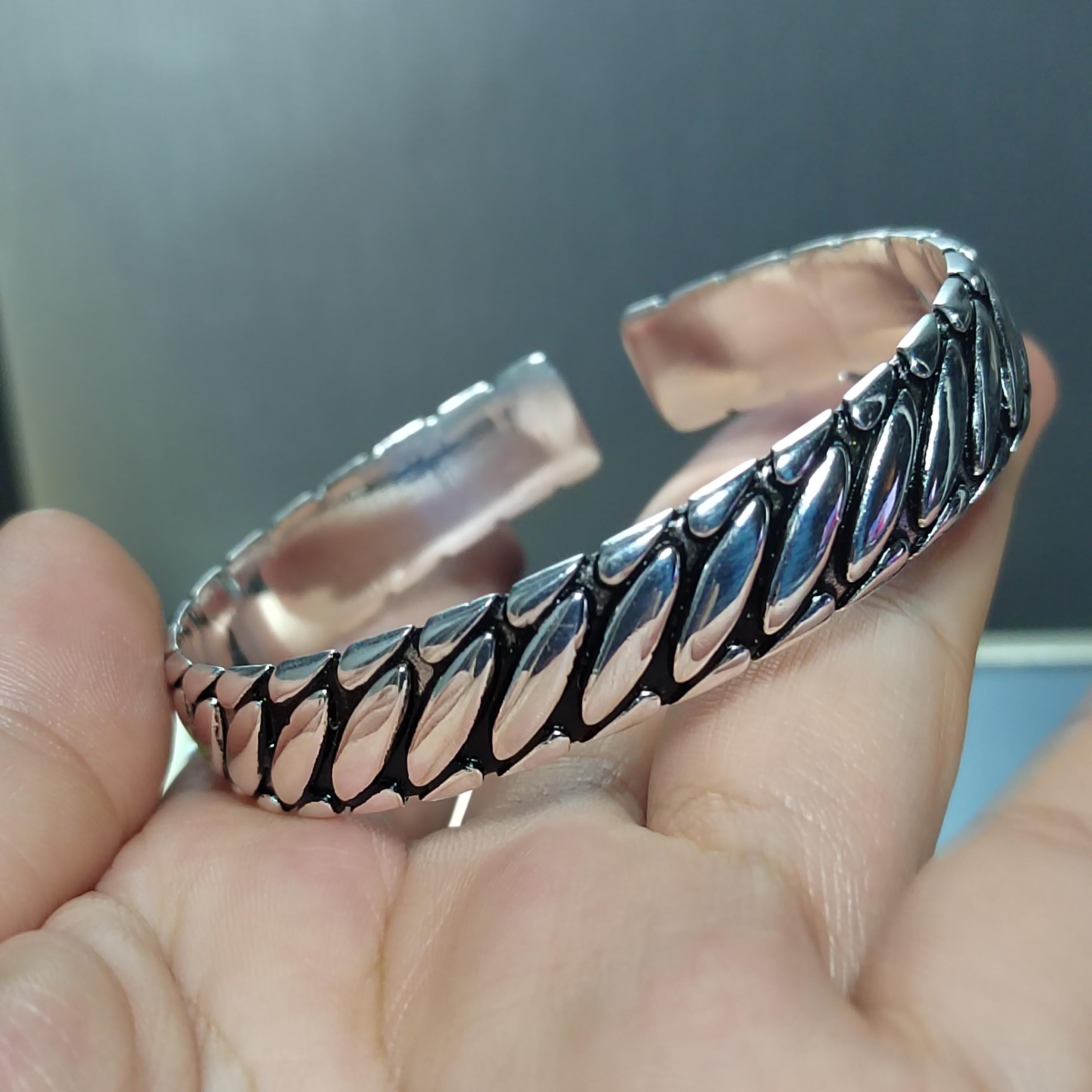 Silver bracelet with leaf-like patterns held in a hand against a blurred background
