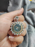 Decorative pendant held in a hand with a blurred gray background