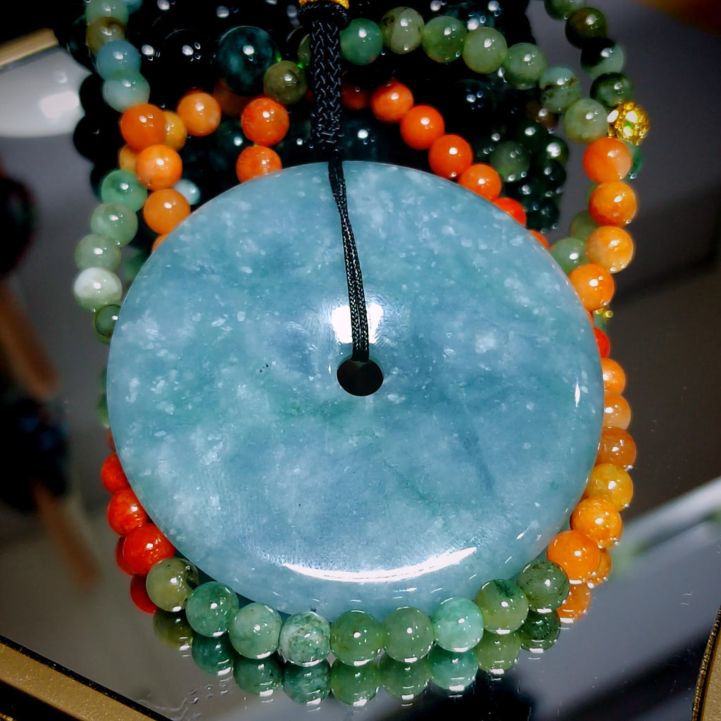 Close-up of a jade pendant on a beaded necklace with a blurred background