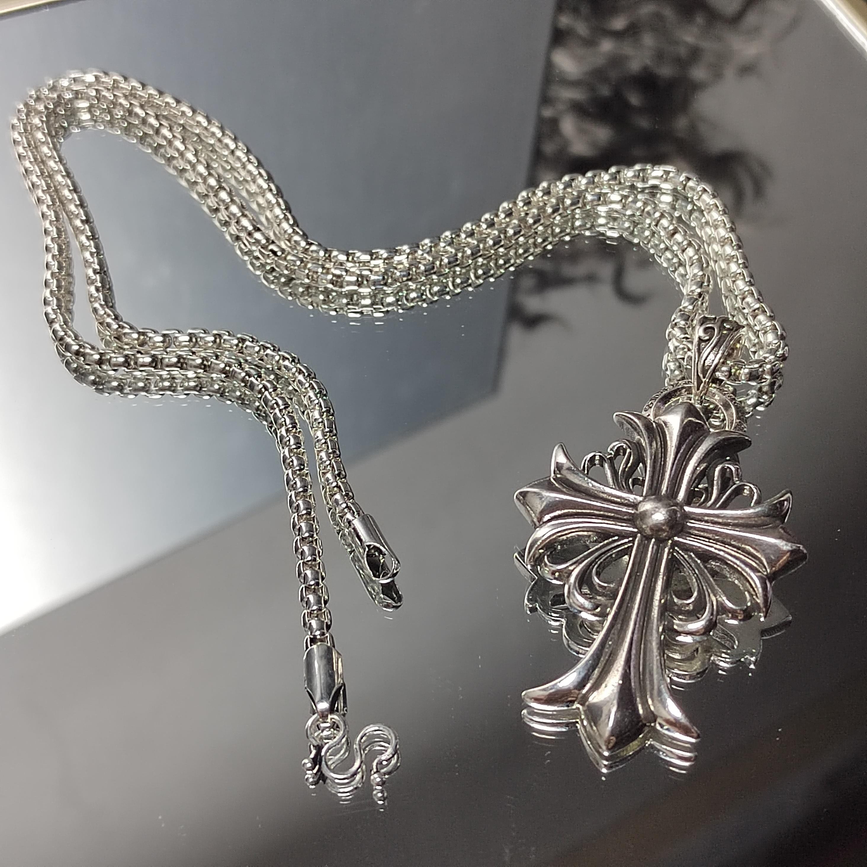 Silver necklace with a detailed cross pendant on a reflective surface