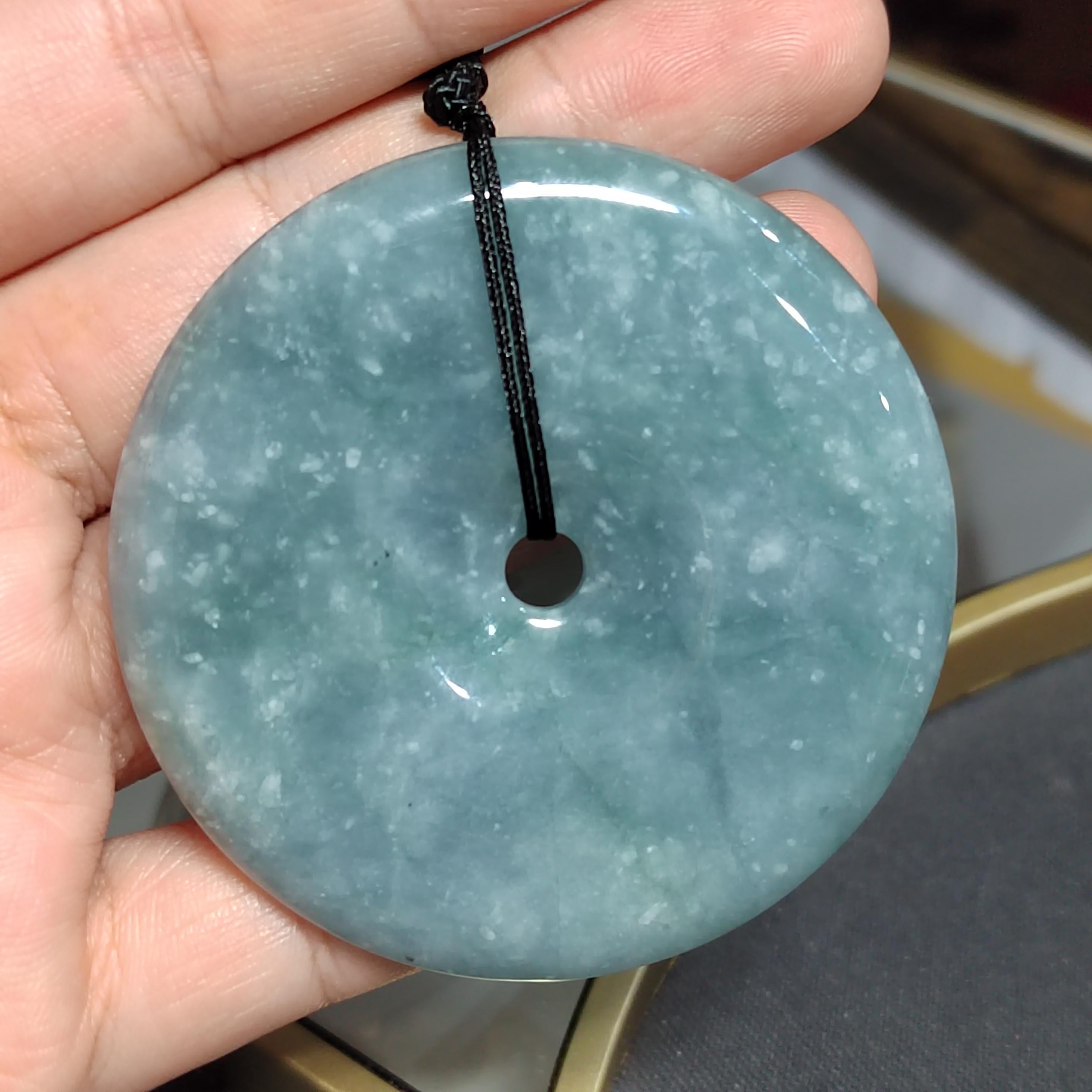 Round jade pendant held in a hand with a blurred background