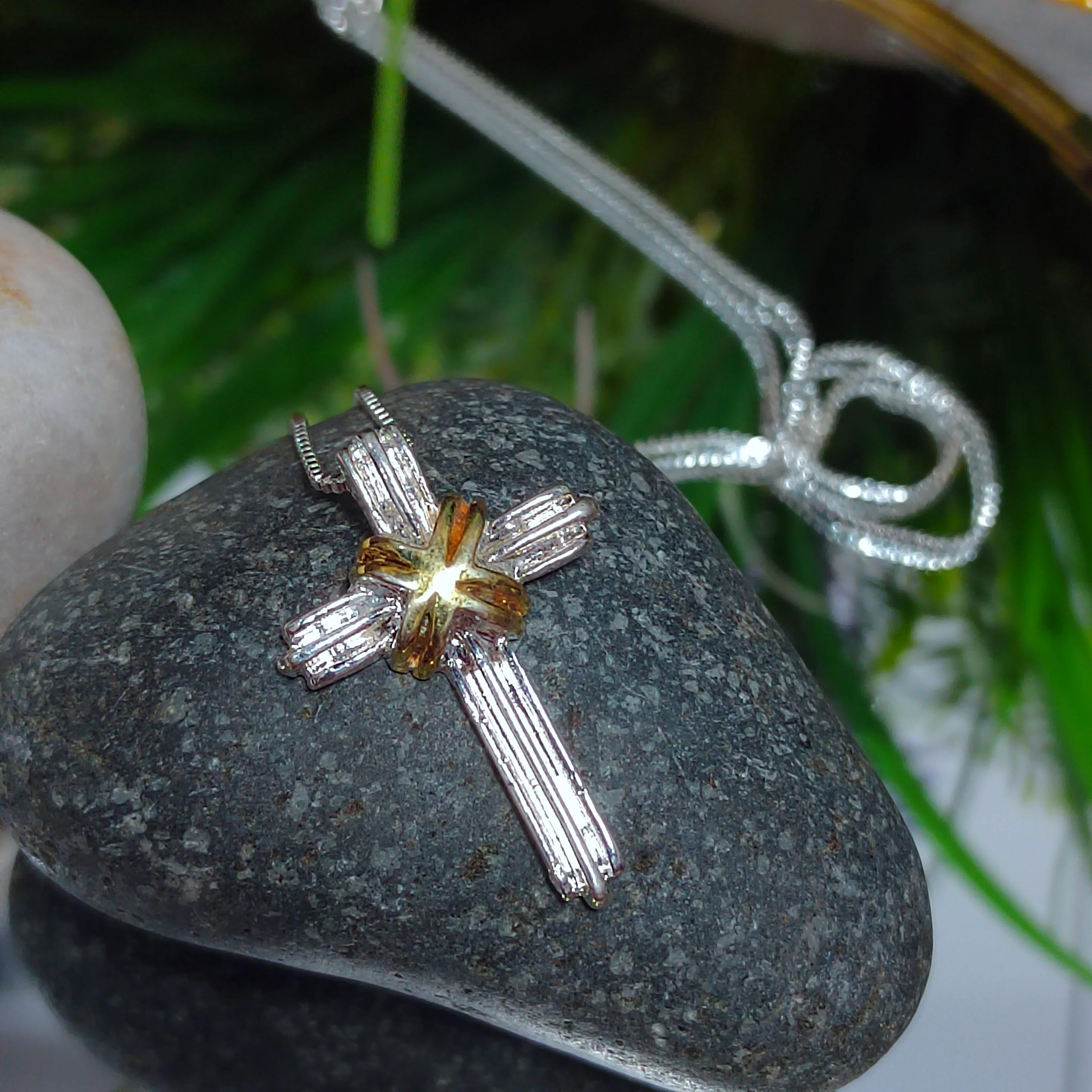 Silver cross pendant with a central gemstone on a gray stone surface