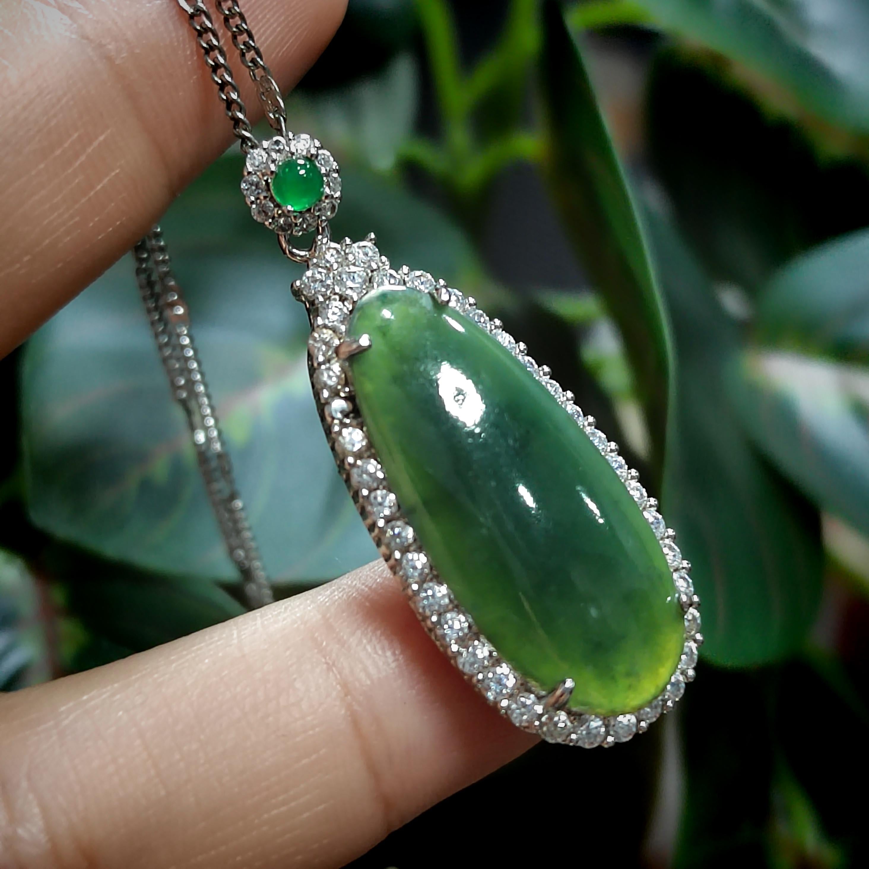 Green jade pendant with diamonds on a finger against a blurred green leafy background