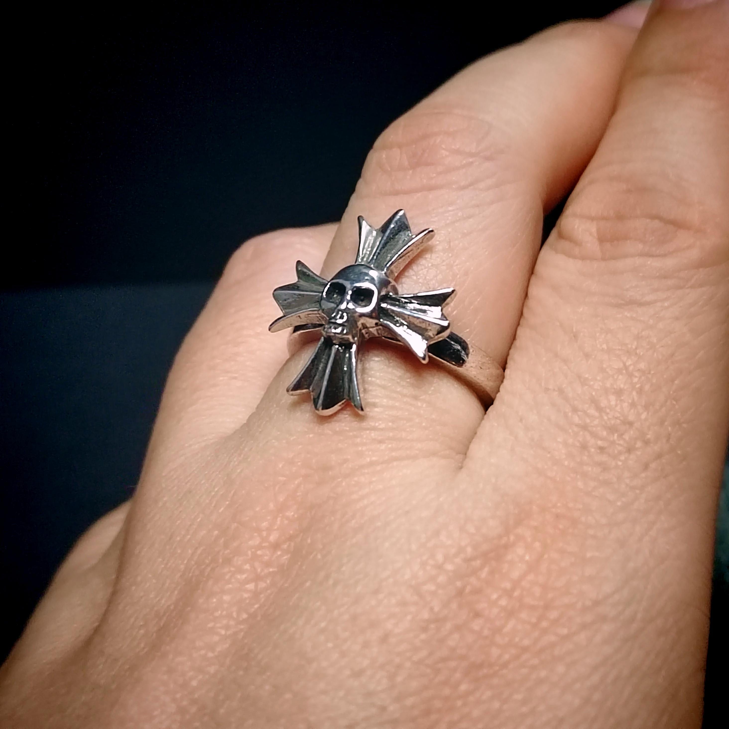 Silver ring with a unique design worn on a finger against a dark background