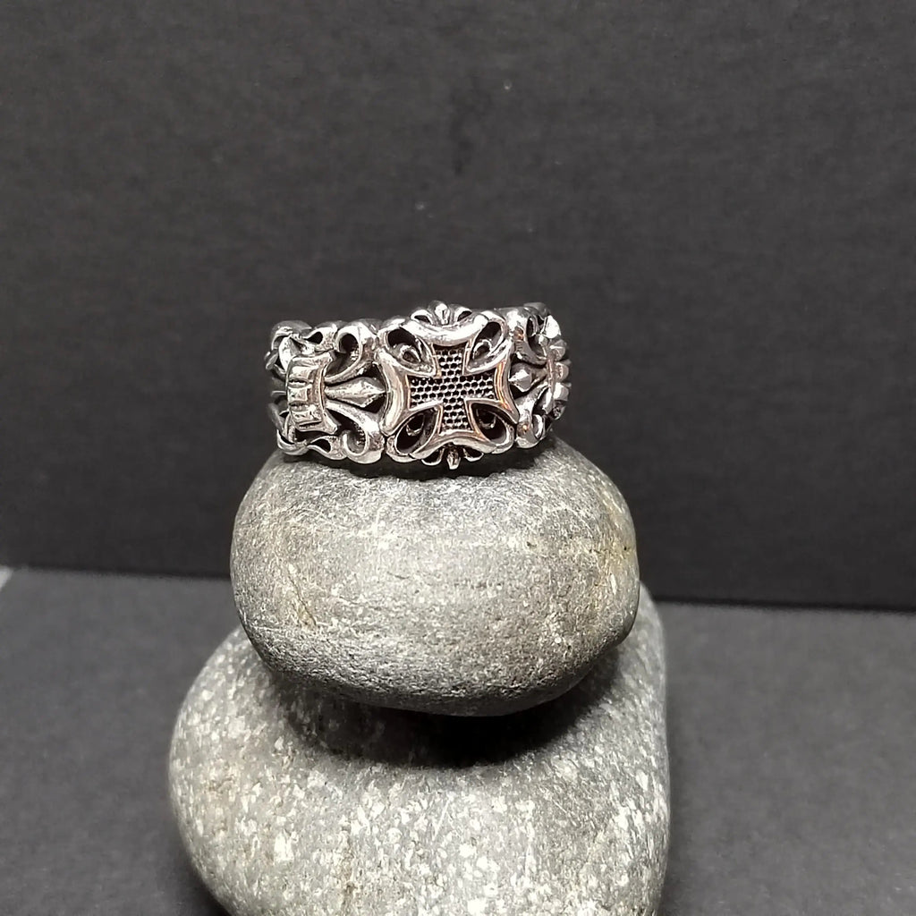 Silver ring with cross design, stacked on two gray stones, against a dark gray background.