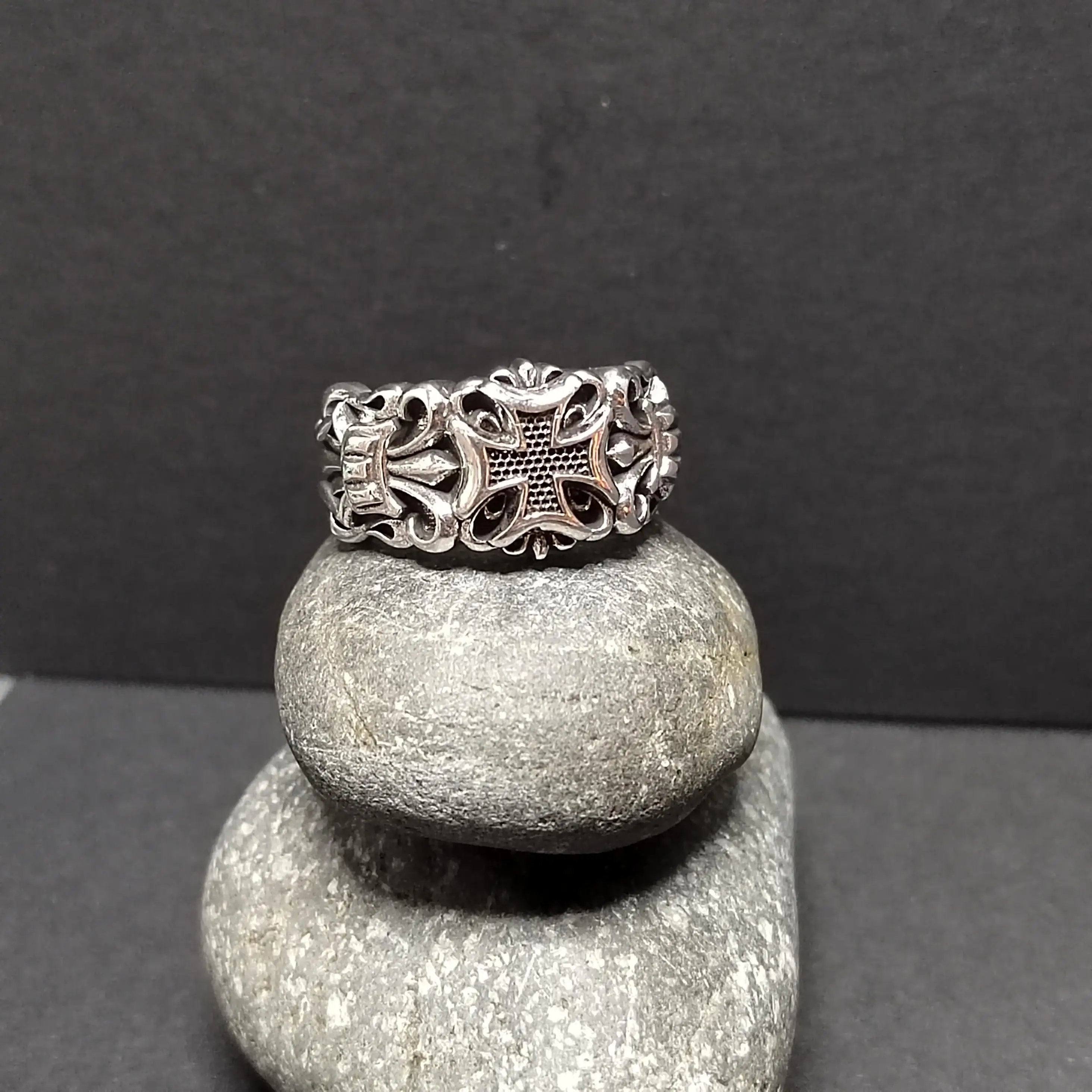 Silver ring with cross design, stacked on two gray stones, against a dark gray background.