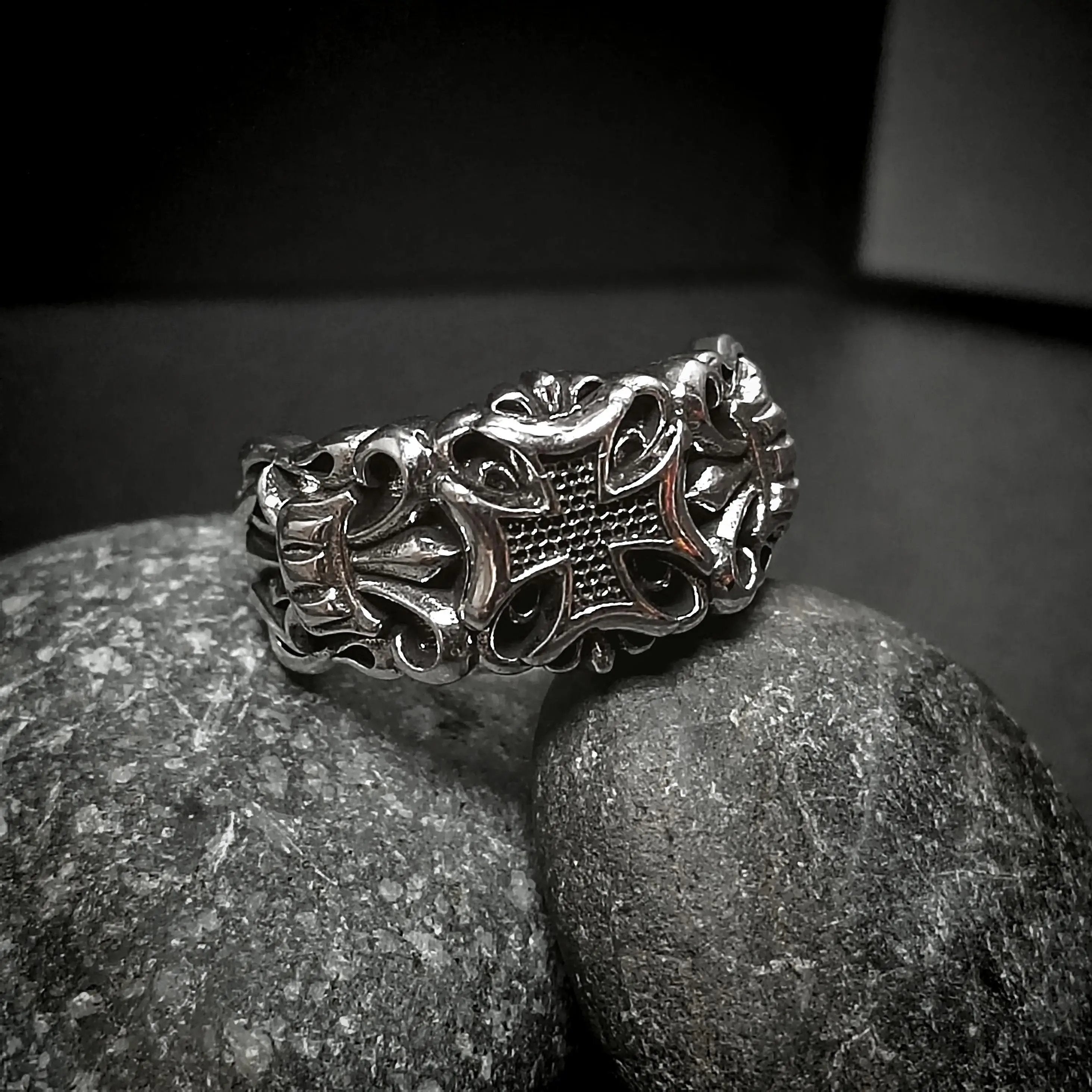 Silver ring with cross design on rocks.