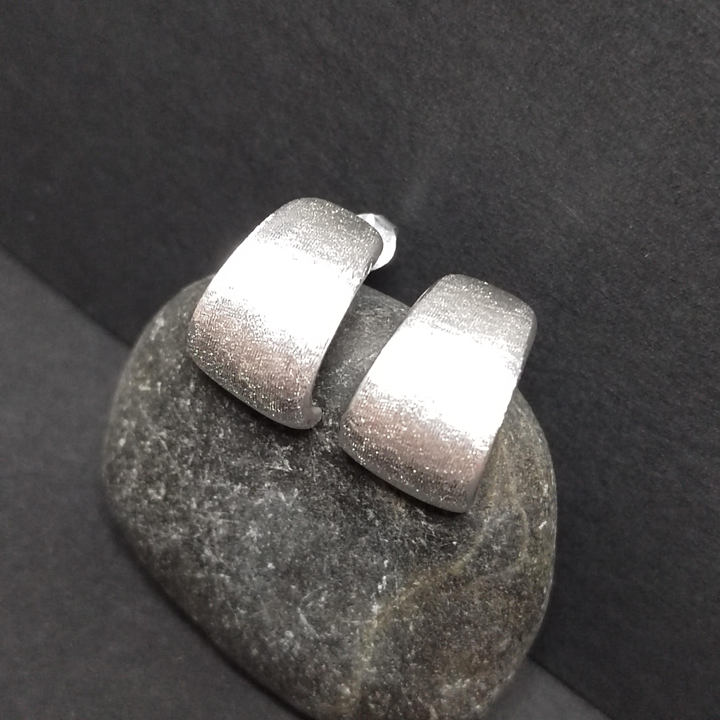 Silver hoop earrings on a dark stone surface