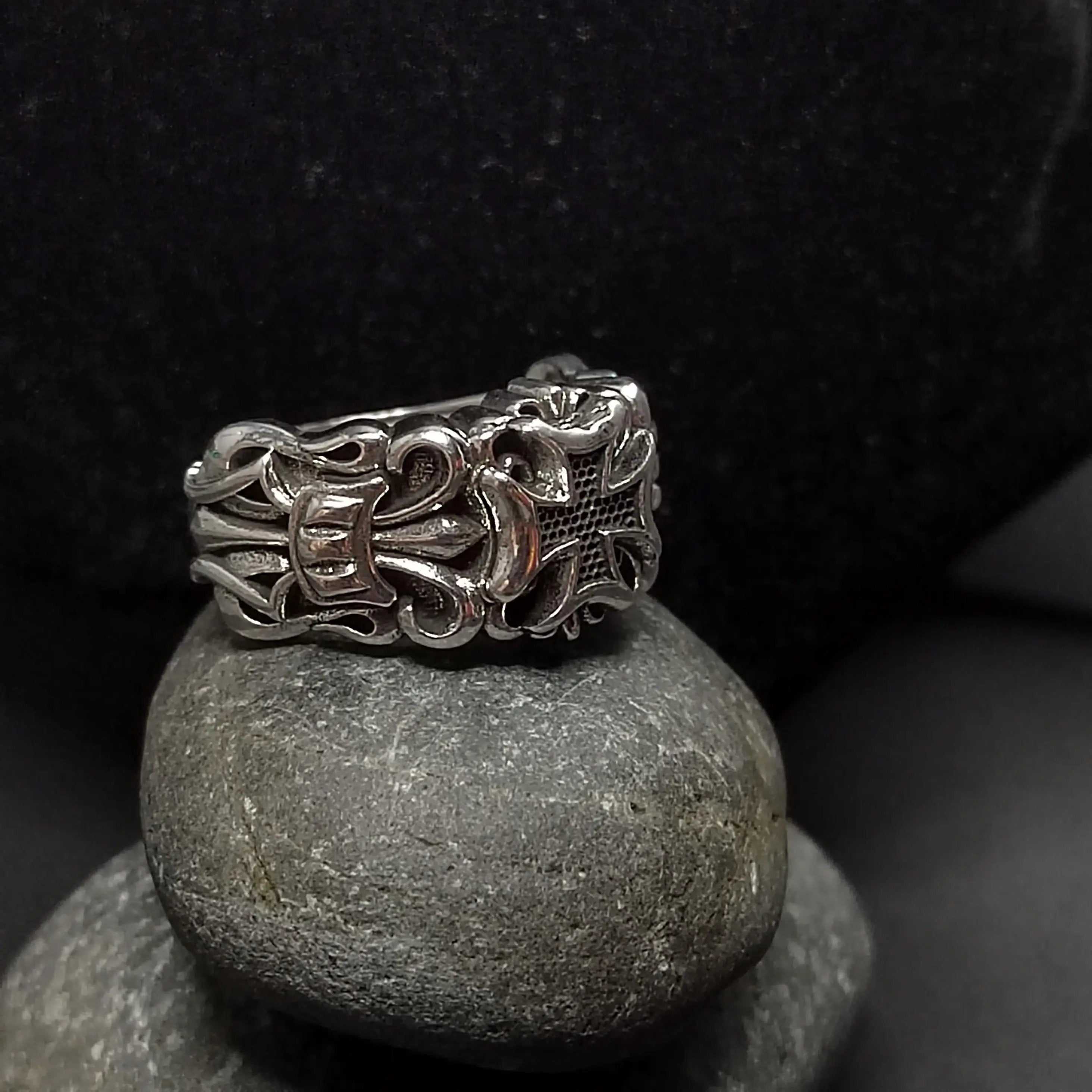 Silver ring with cross design on gray stones against a black background.