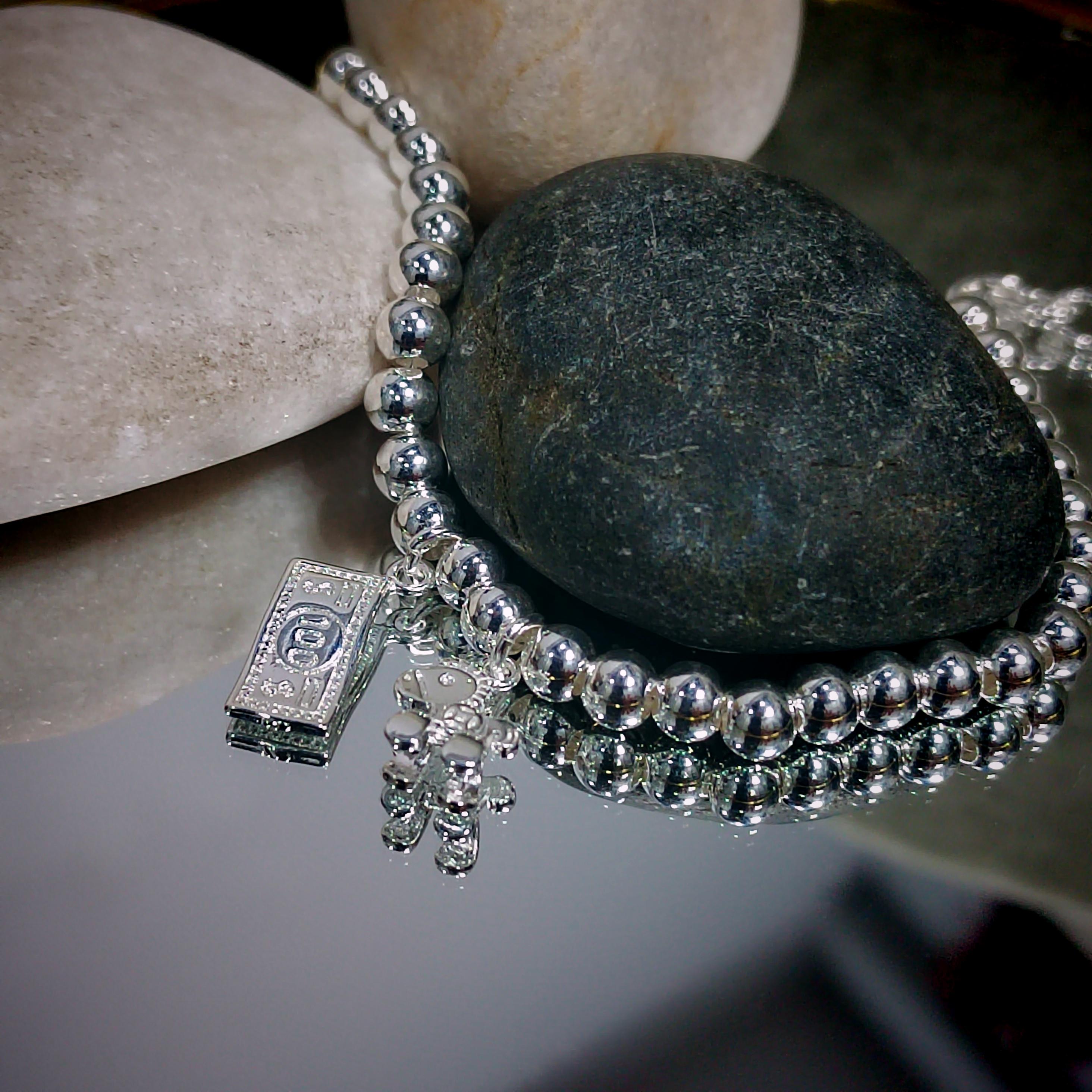 Silver beaded bracelet with charms on a stone surface