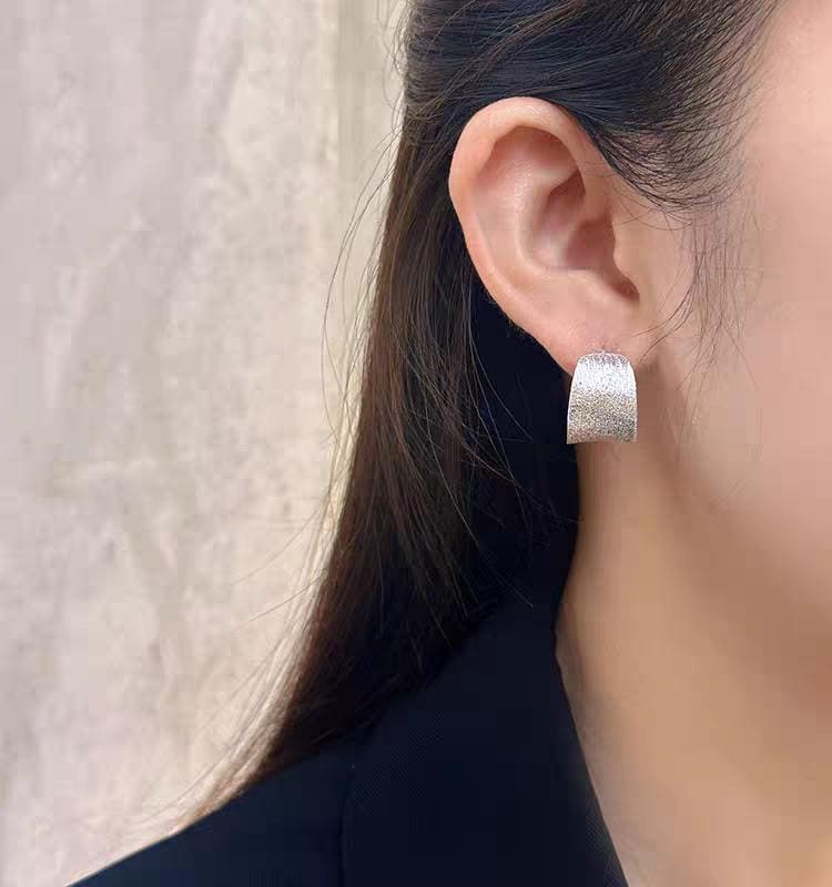 Silver hoop earring worn by a person with a neutral background