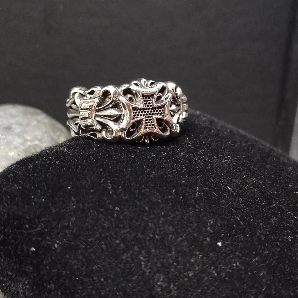 Silver ring with ornate floral and cross design, resting on black velvet.
