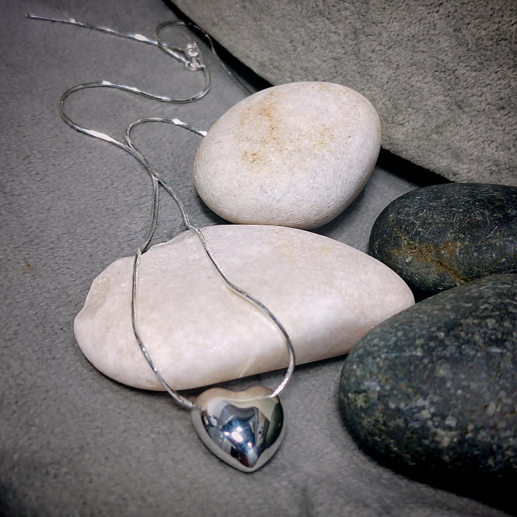 Silver heart-shaped pendant necklace on pebbles