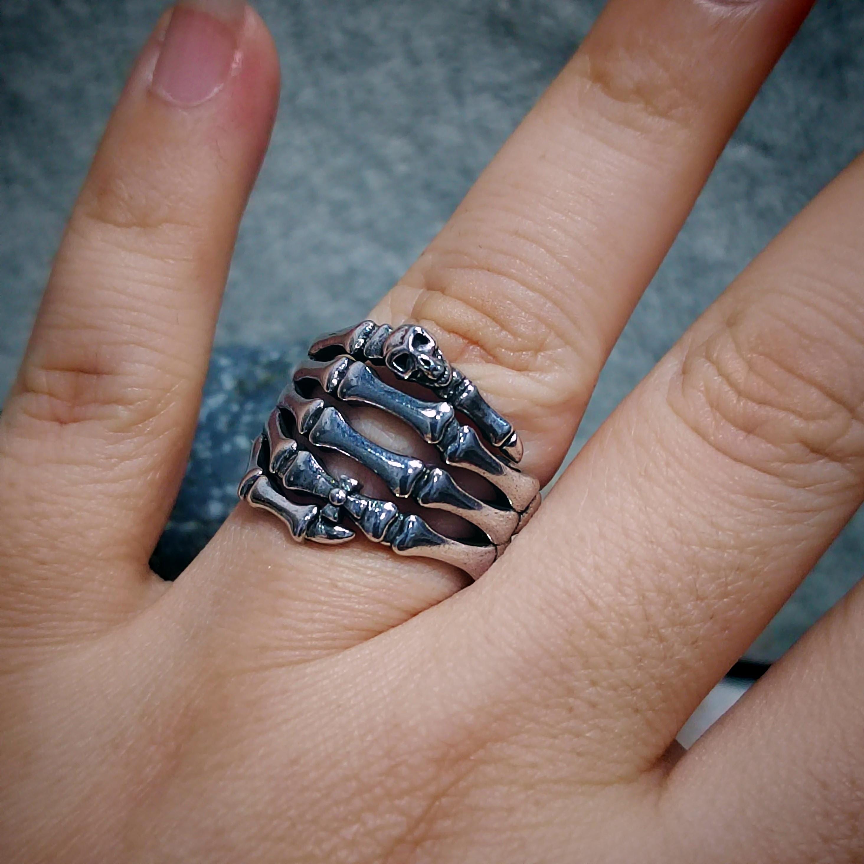 Silver skeleton hand ring on a finger with a blurred background