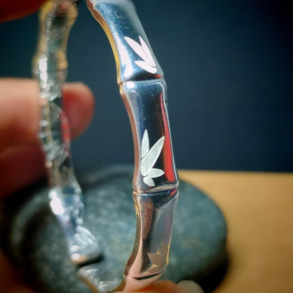 Close-up of a hand holding a glass pipe with leaf designs against a blurred background