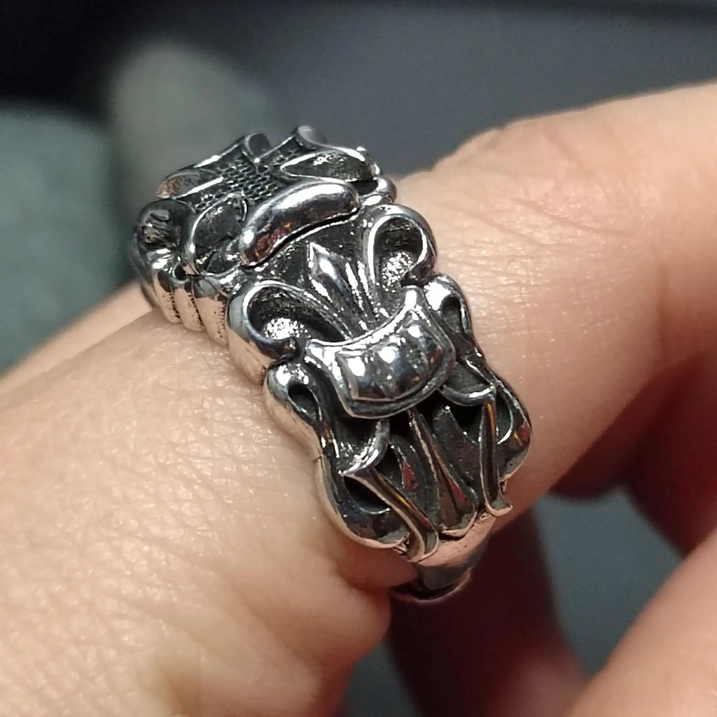 A silver ring with a fleur-de-lis design on a finger.