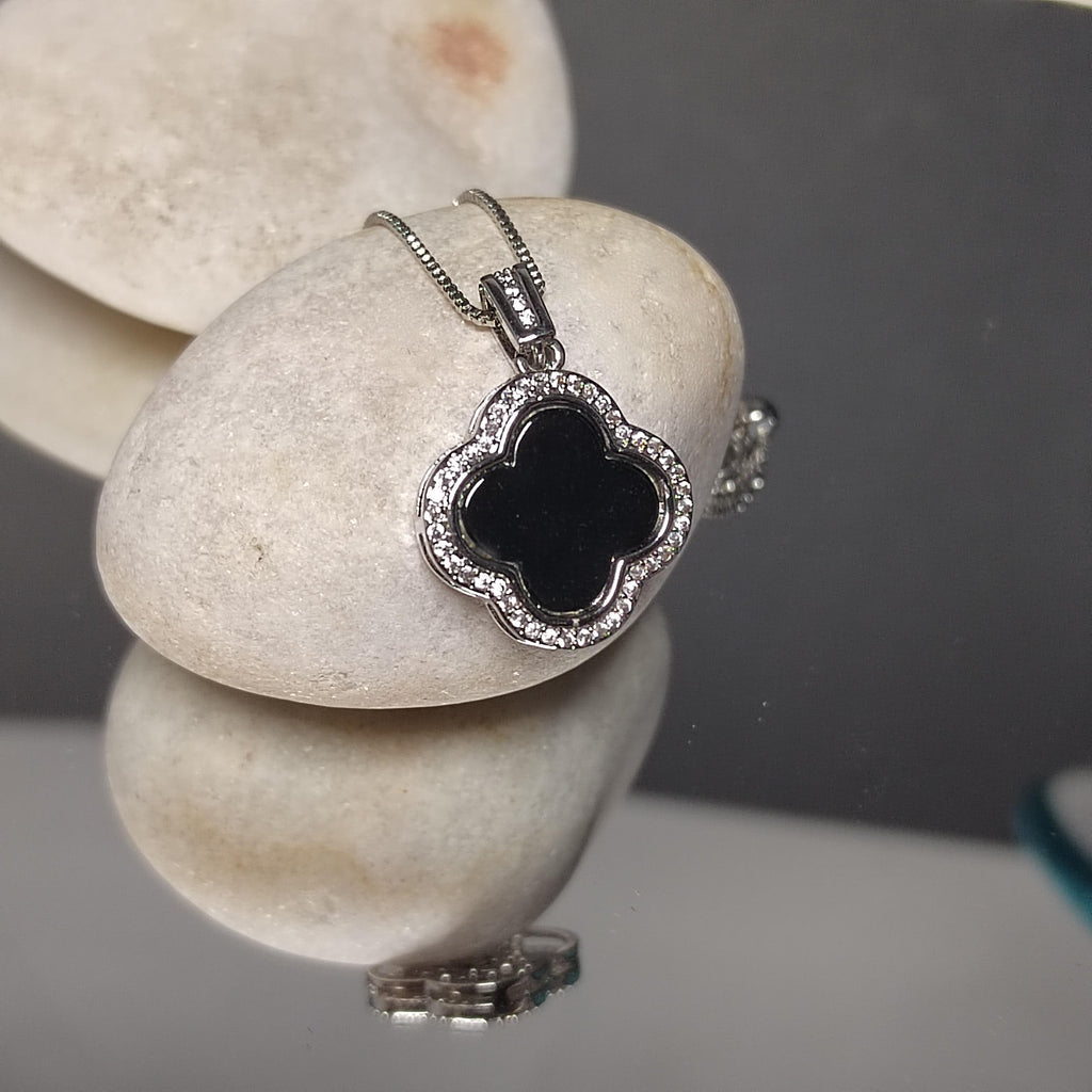 Silver necklace with a black clover pendant on a stone surface