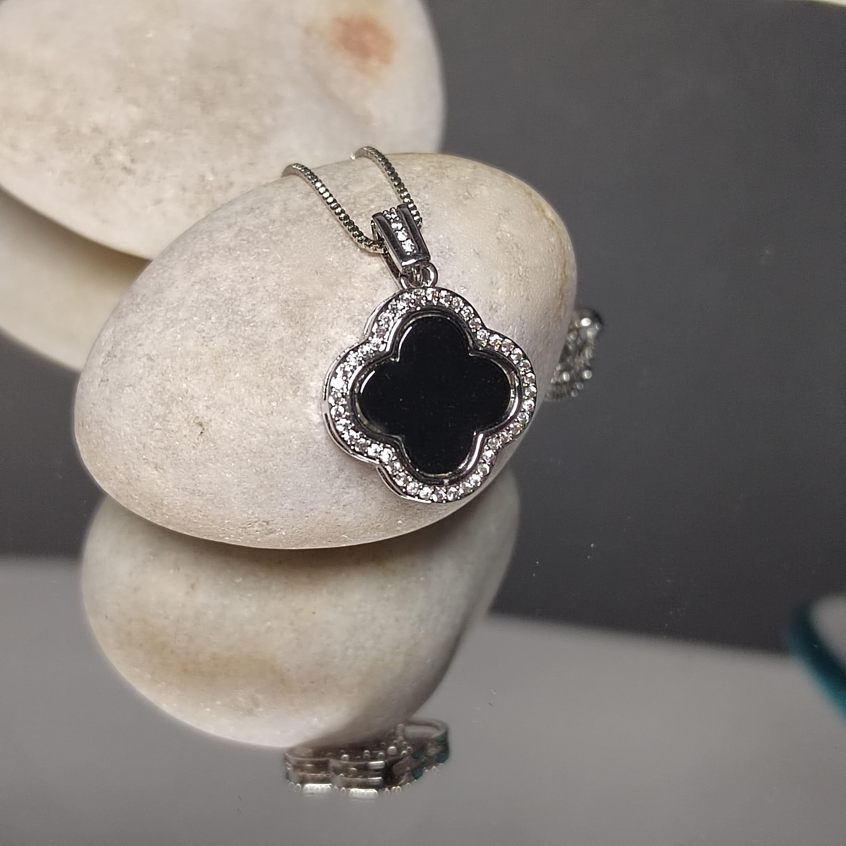 Silver necklace with a black clover pendant on a stone surface