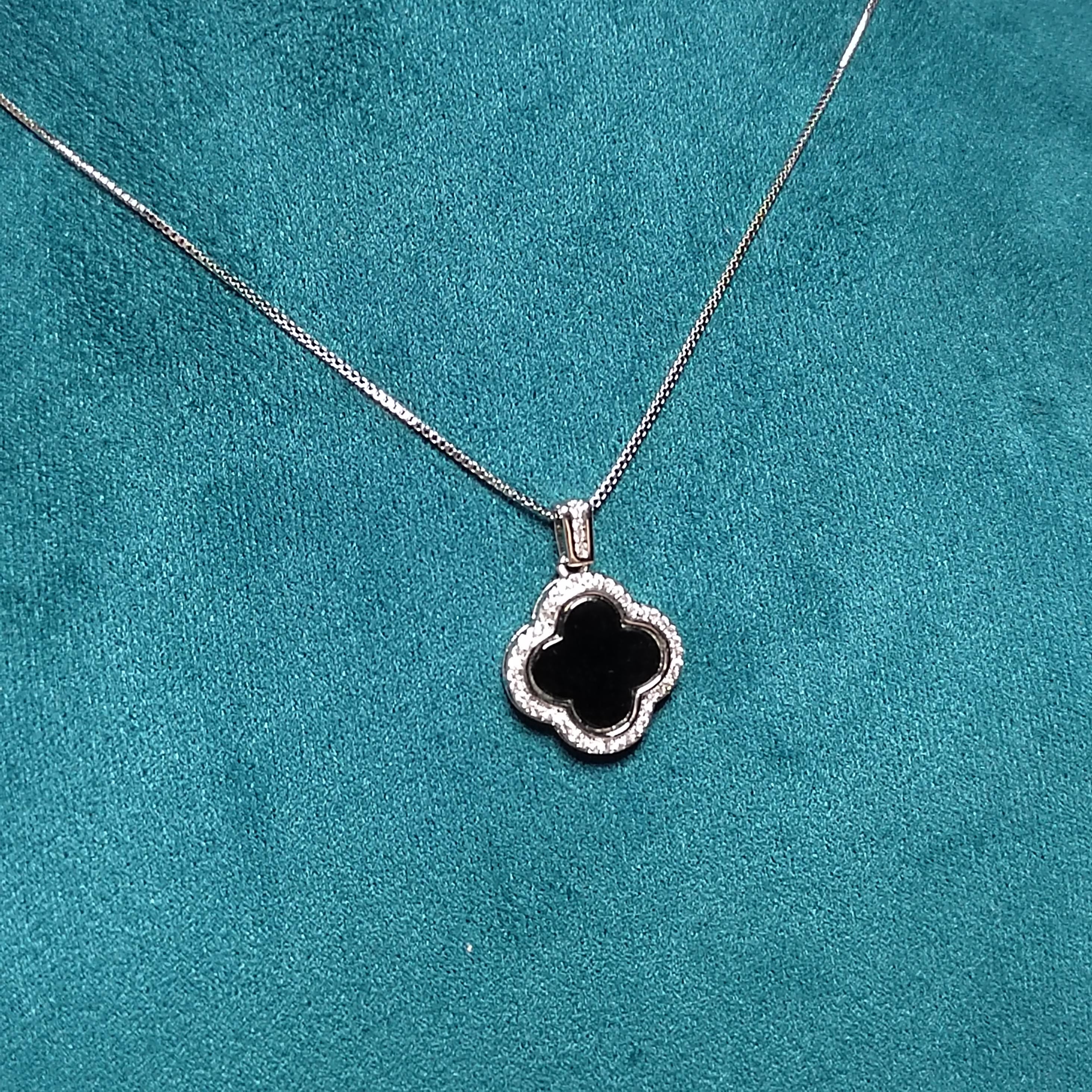 Silver necklace with a clover-shaped pendant on a teal background