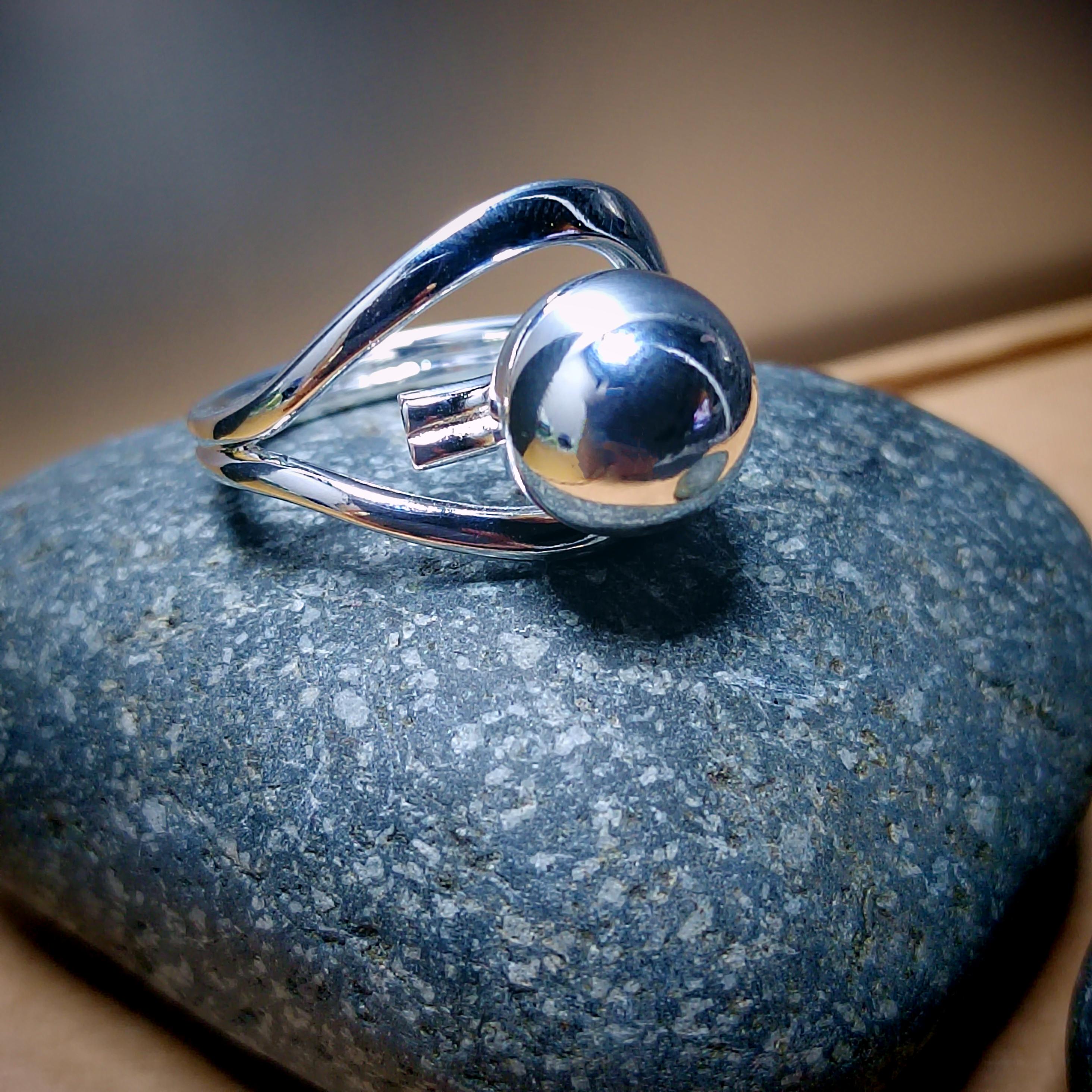 Silver ring with a spherical design on a textured stone surface