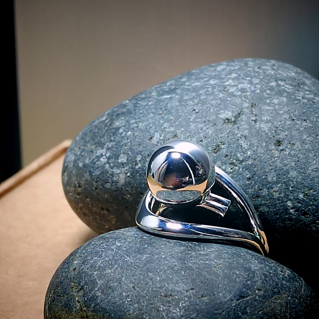 Silver ring with a spherical design on a textured stone surface