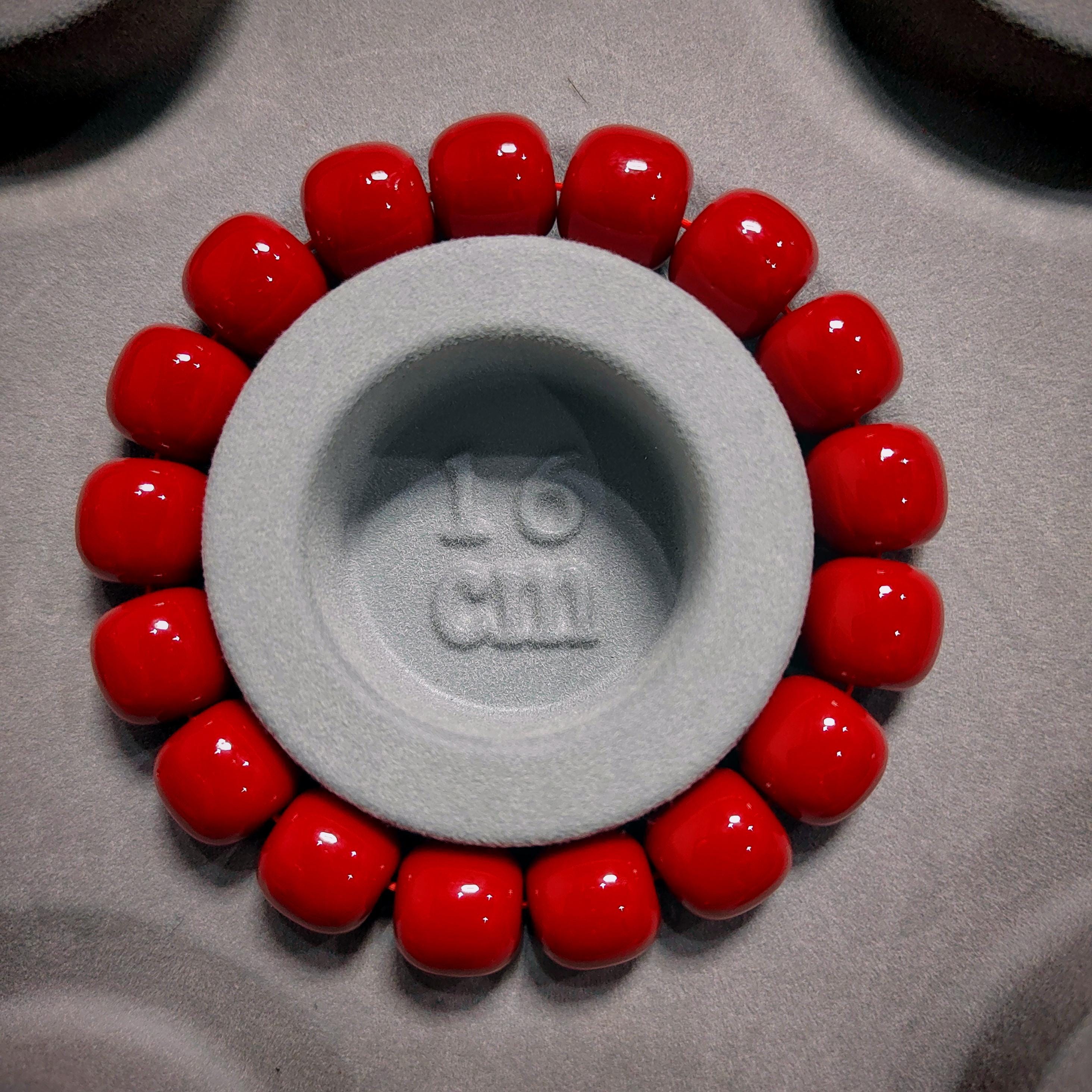 Gray circular object with '16 cm' marking surrounded by red beads on a gray background