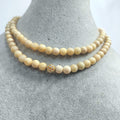 Beige beaded necklace with a gold clasp on a gray surface