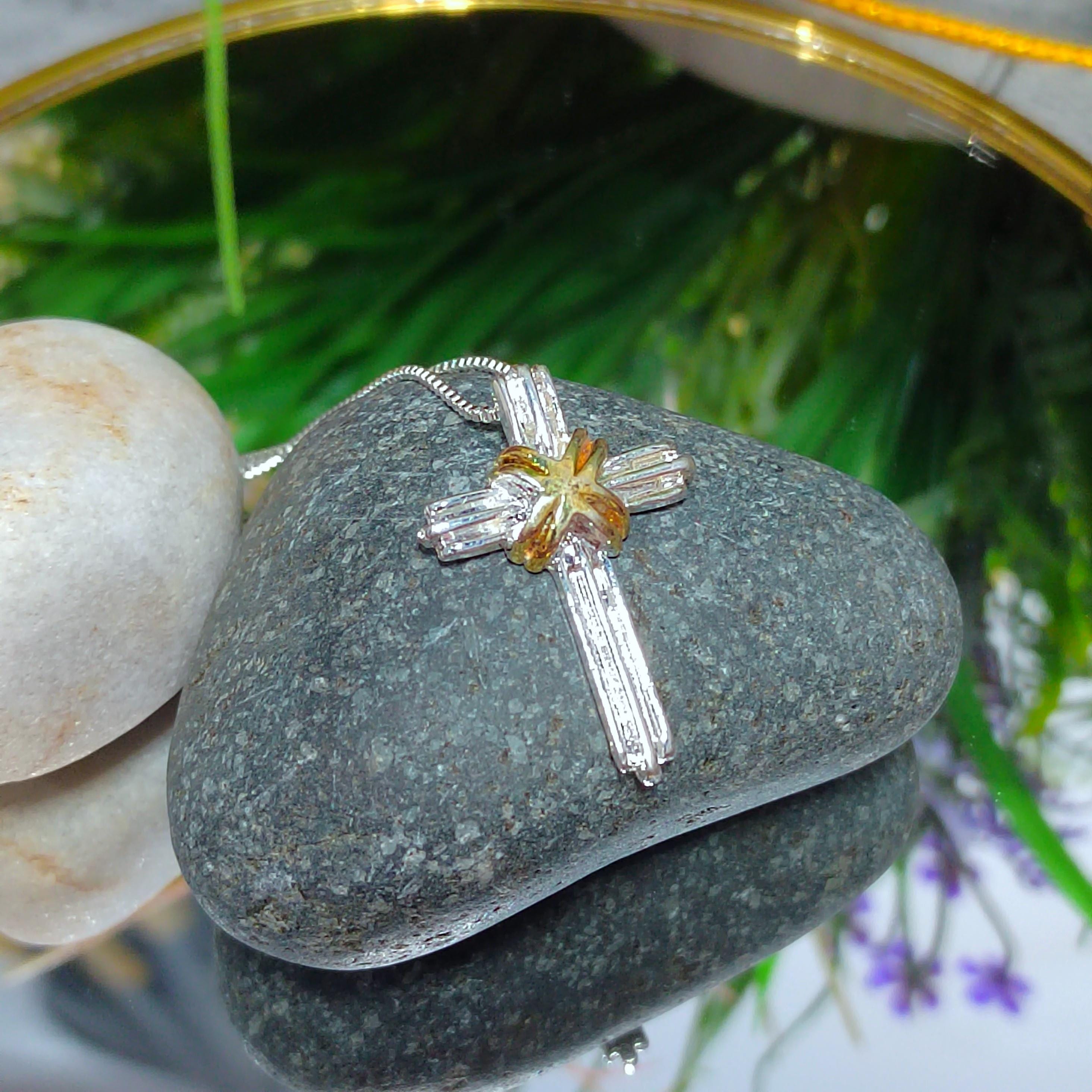 Silver cross pendant on a rock with blurred greenery in the background