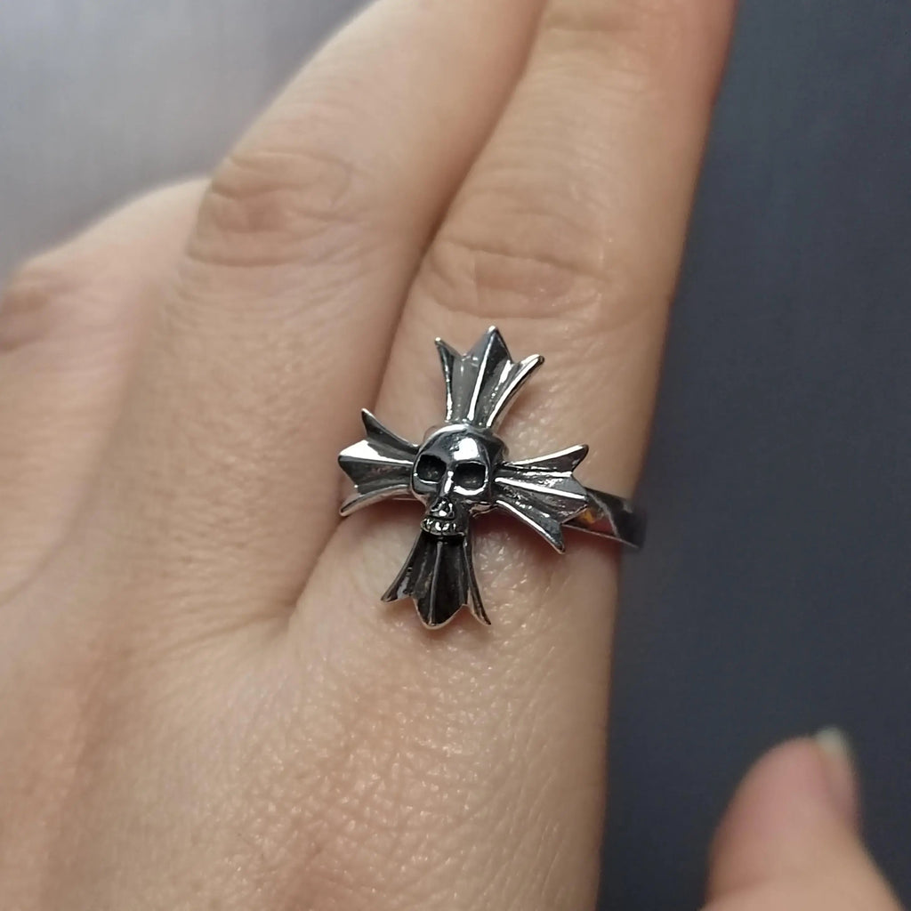 Silver skull and crossbones ring on a finger with a neutral background
