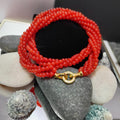 Luxurious twisted red agate bead necklace with gold-plated clasp, displayed on smooth stones, elegant and vibrant design.