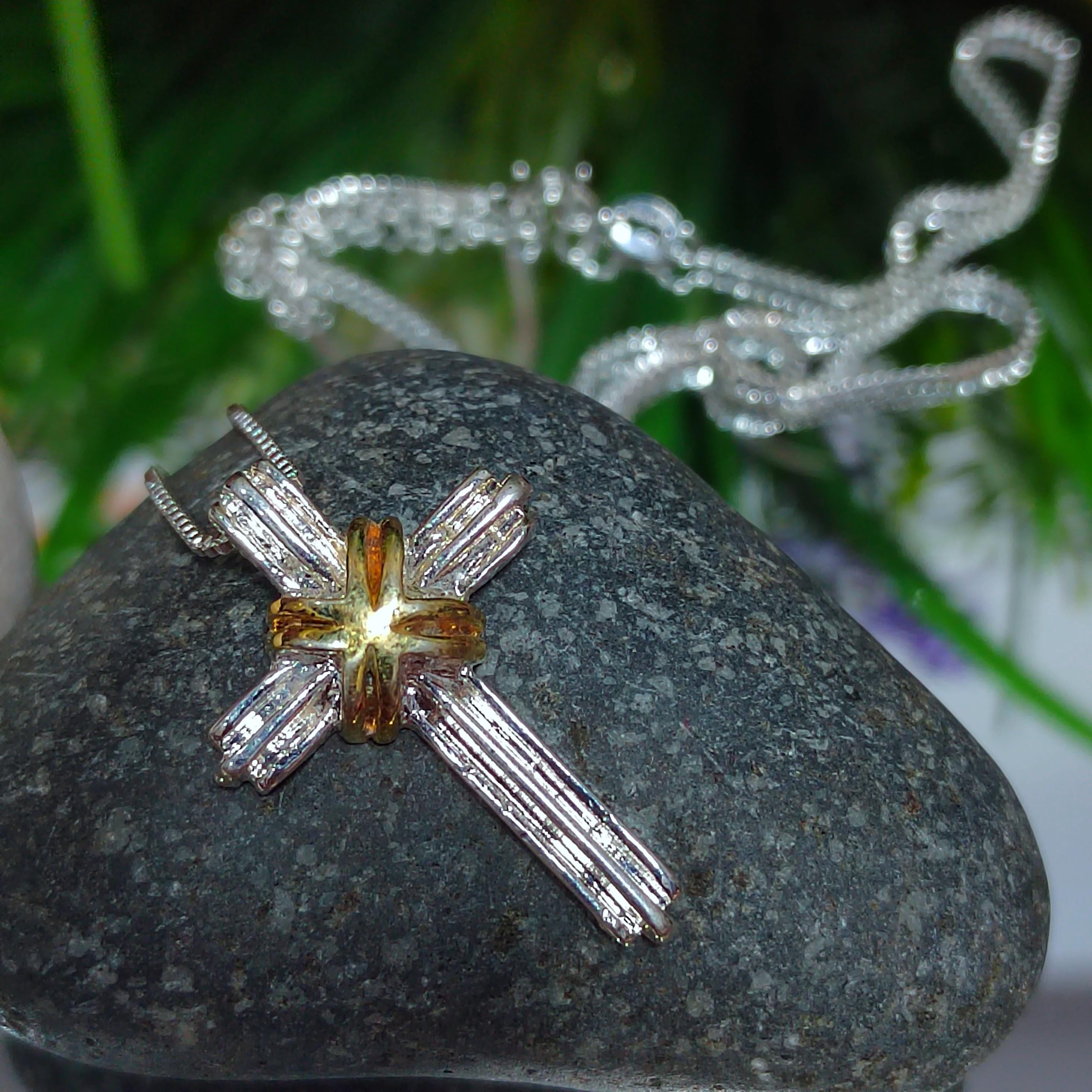 Silver cross-shaped pendant on a stone with blurred greenery in the background