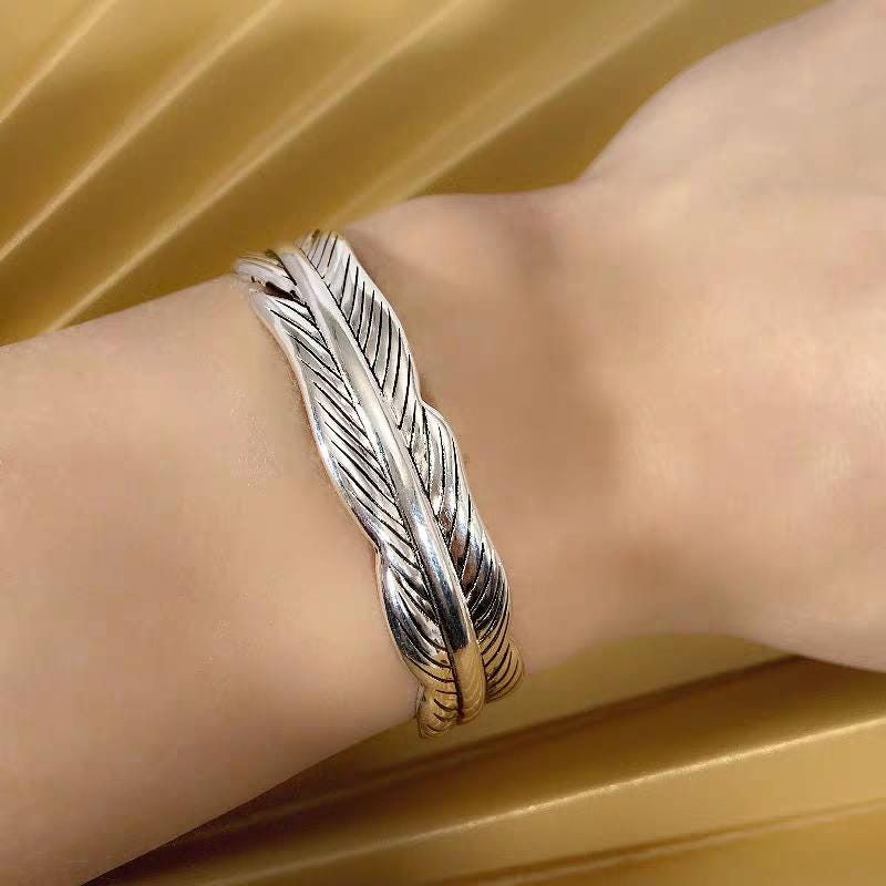 Silver feather-shaped bracelet on a wrist against a gold background