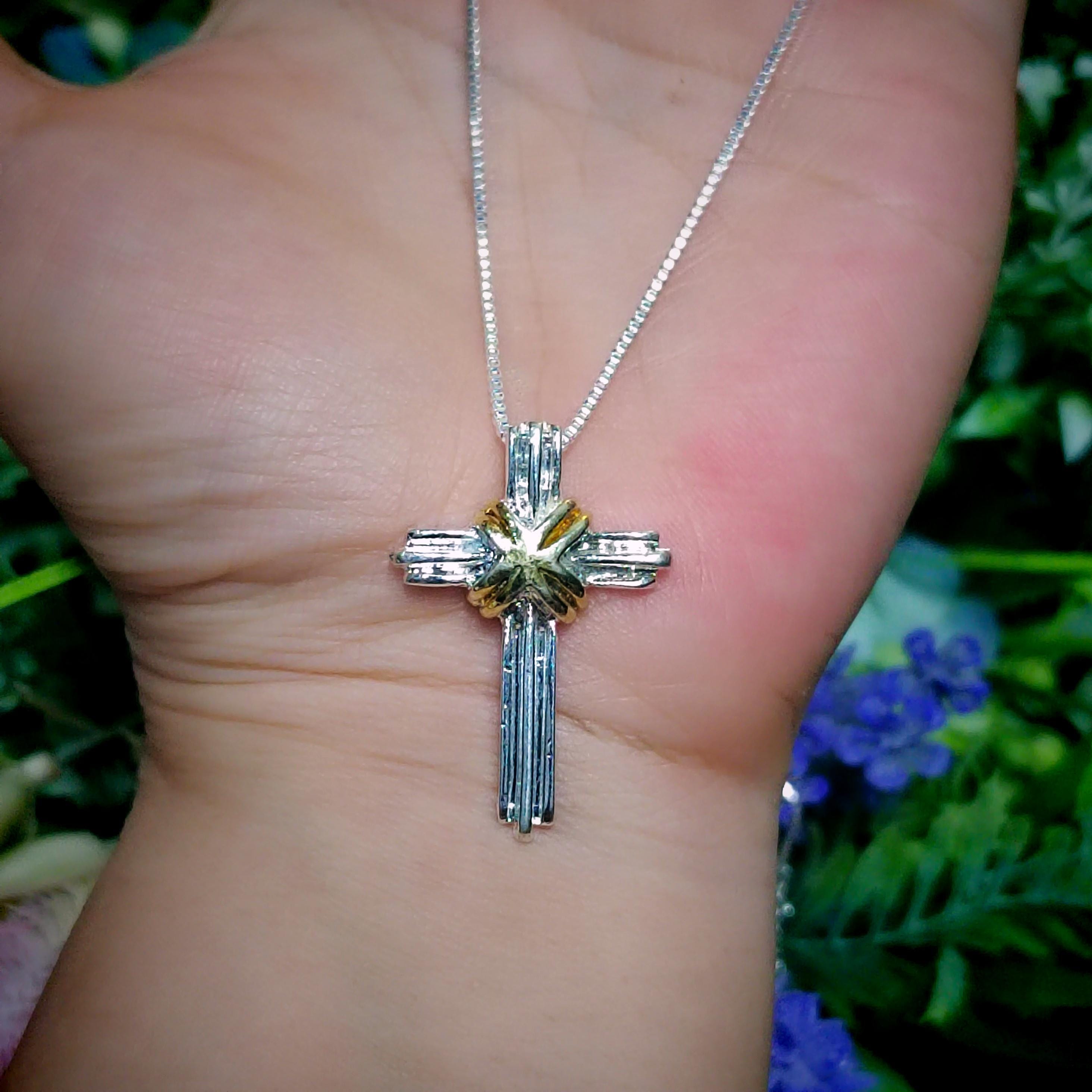 Silver cross necklace on a hand with a blurred natural background