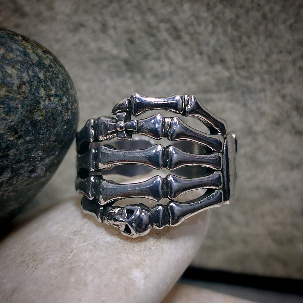 Silver skeleton hand ring on a person's finger with a stone background