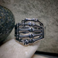 Silver skeleton hand ring on a person's finger with a stone background