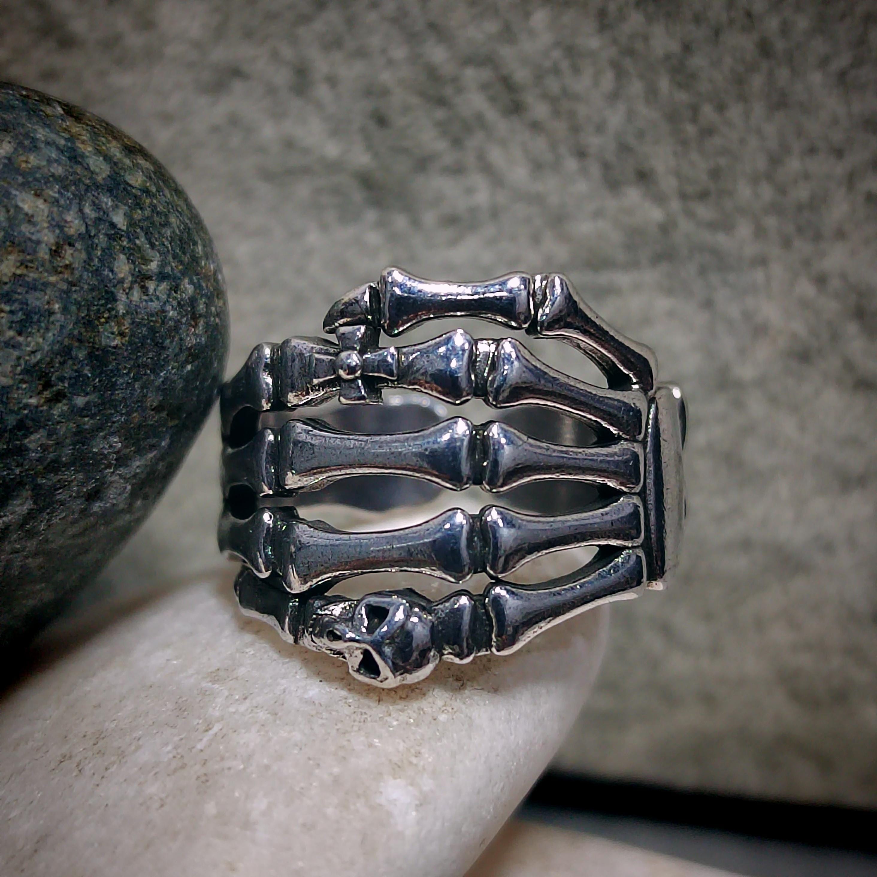 Silver skeleton hand ring on a person's finger with a stone background