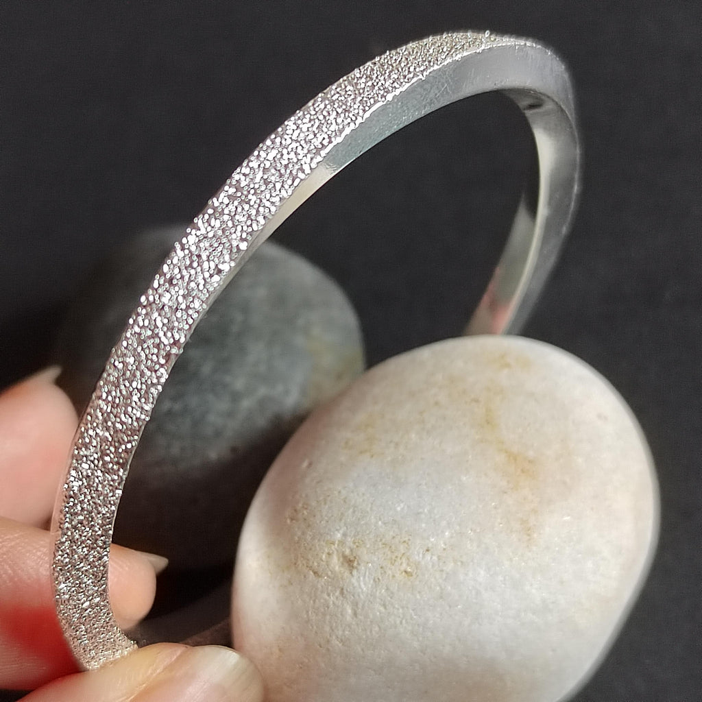 Silver bracelet held over a stone with a dark background