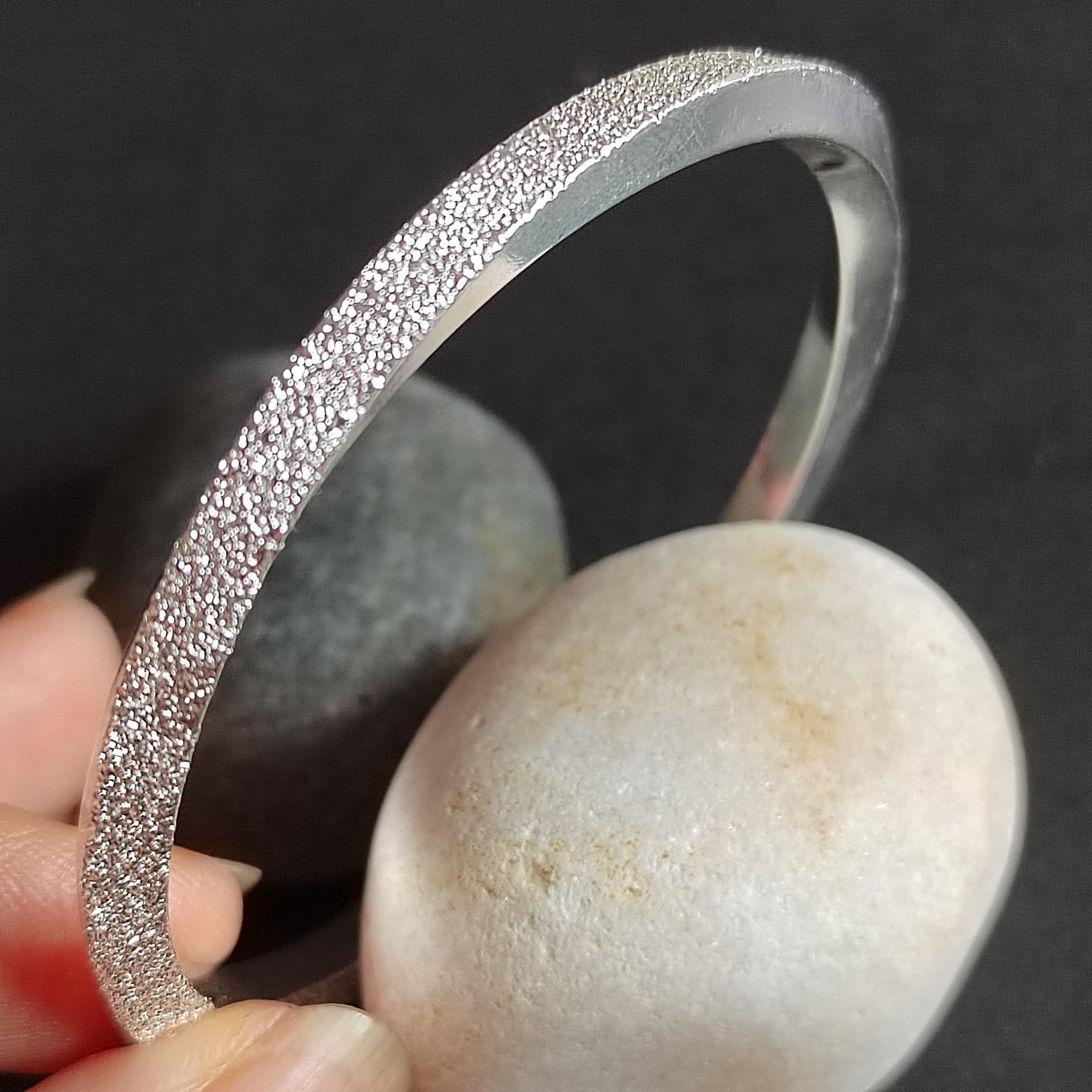 Silver bracelet held over a stone with a dark background