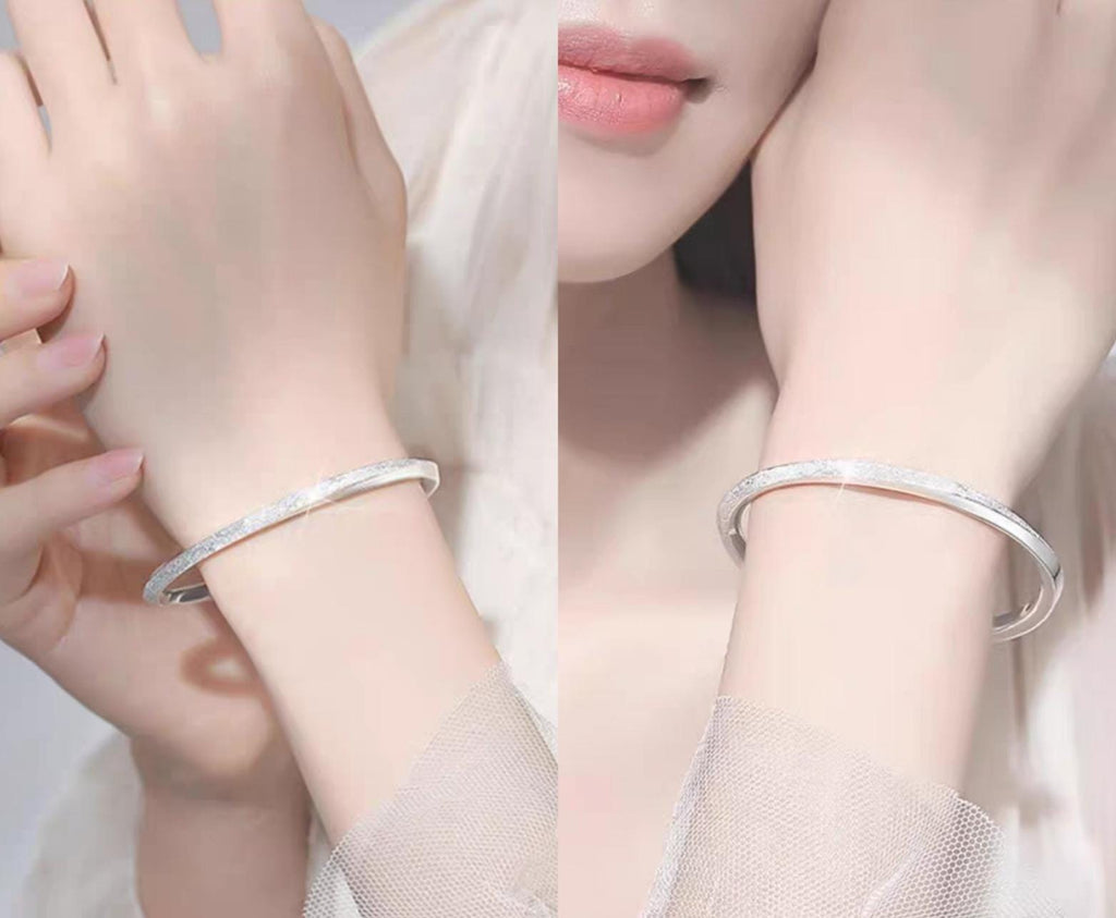 Close-up of a person wearing a silver bracelet on a light background