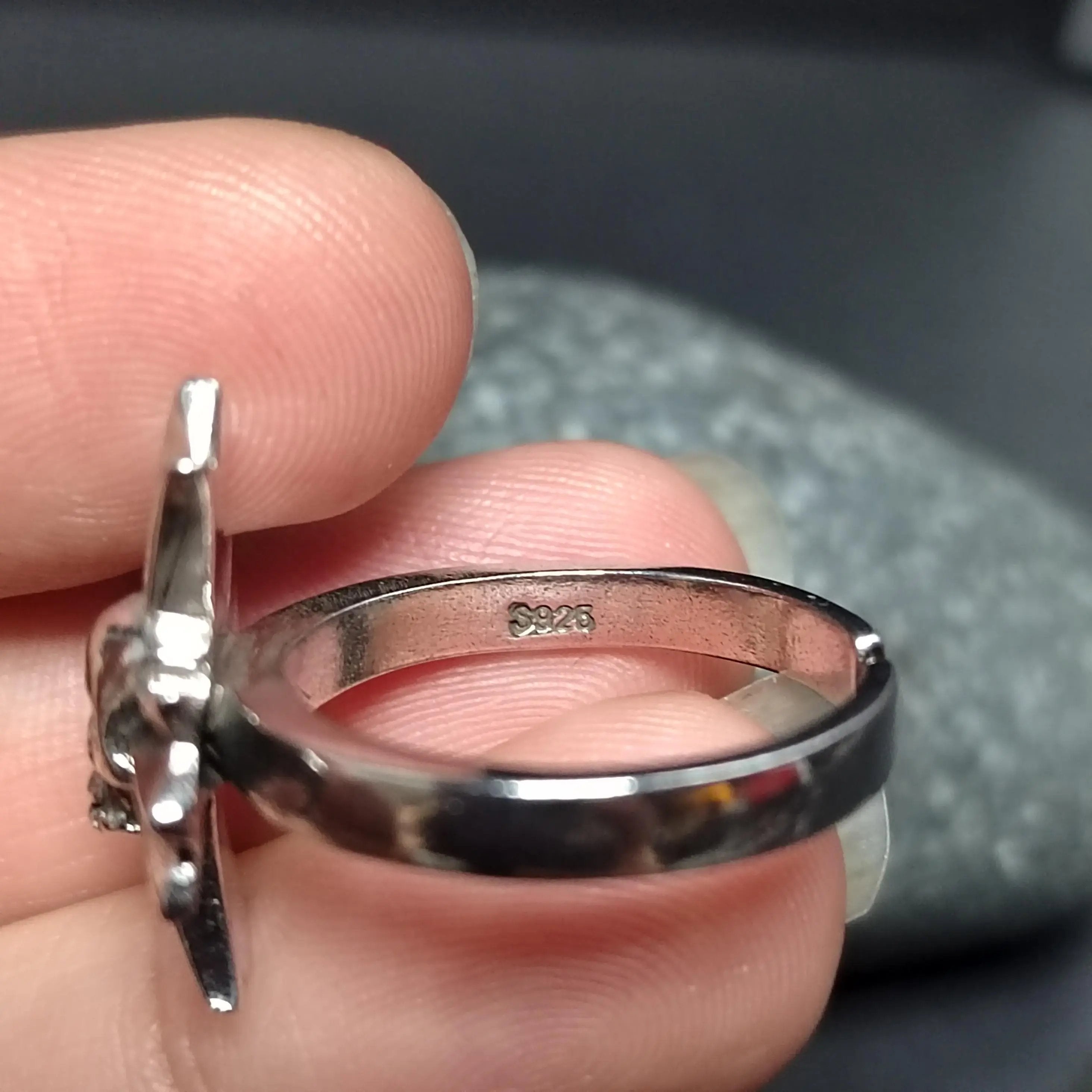 Silver ring with a unique design held between fingers against a blurred background