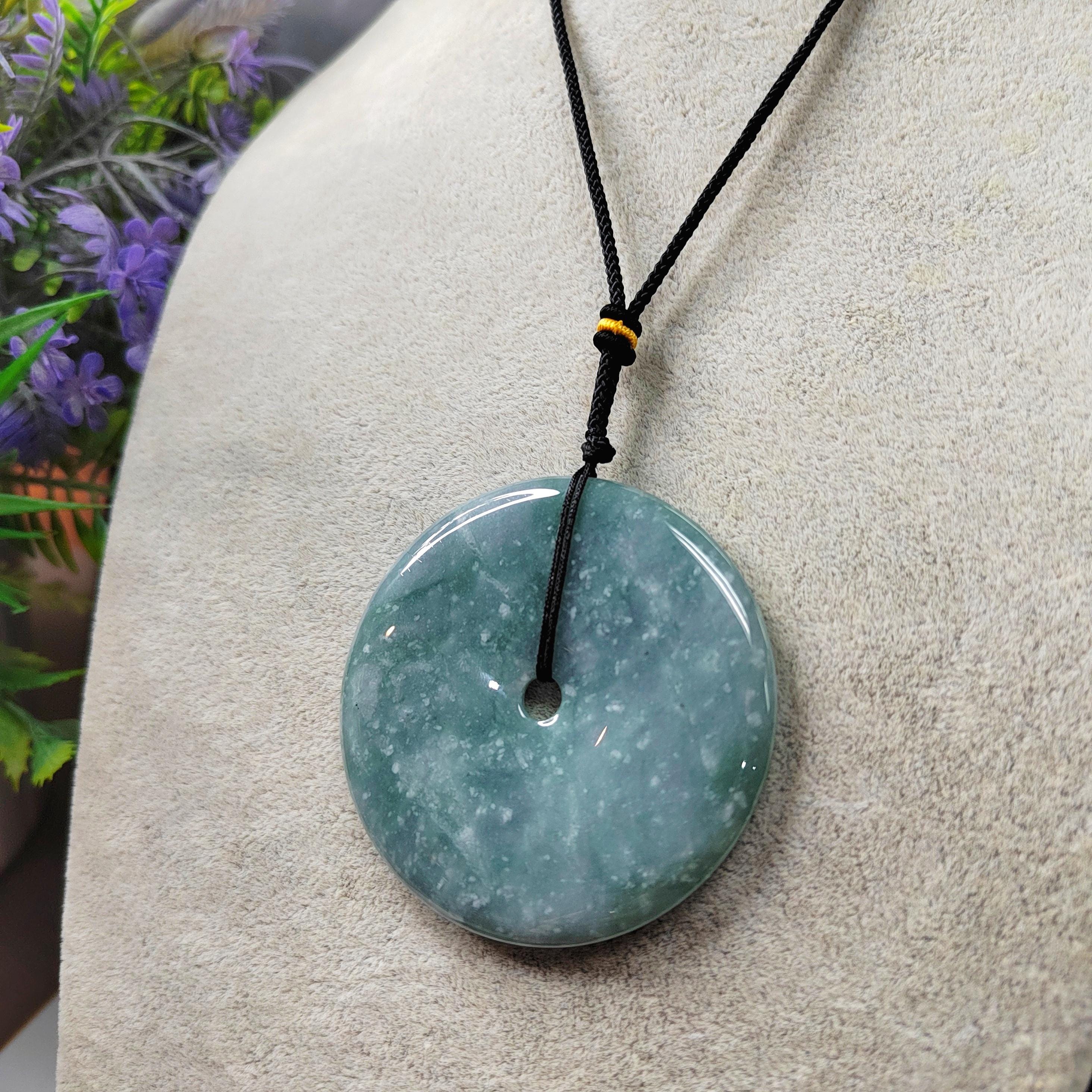 Green stone pendant on a black cord against a neutral background