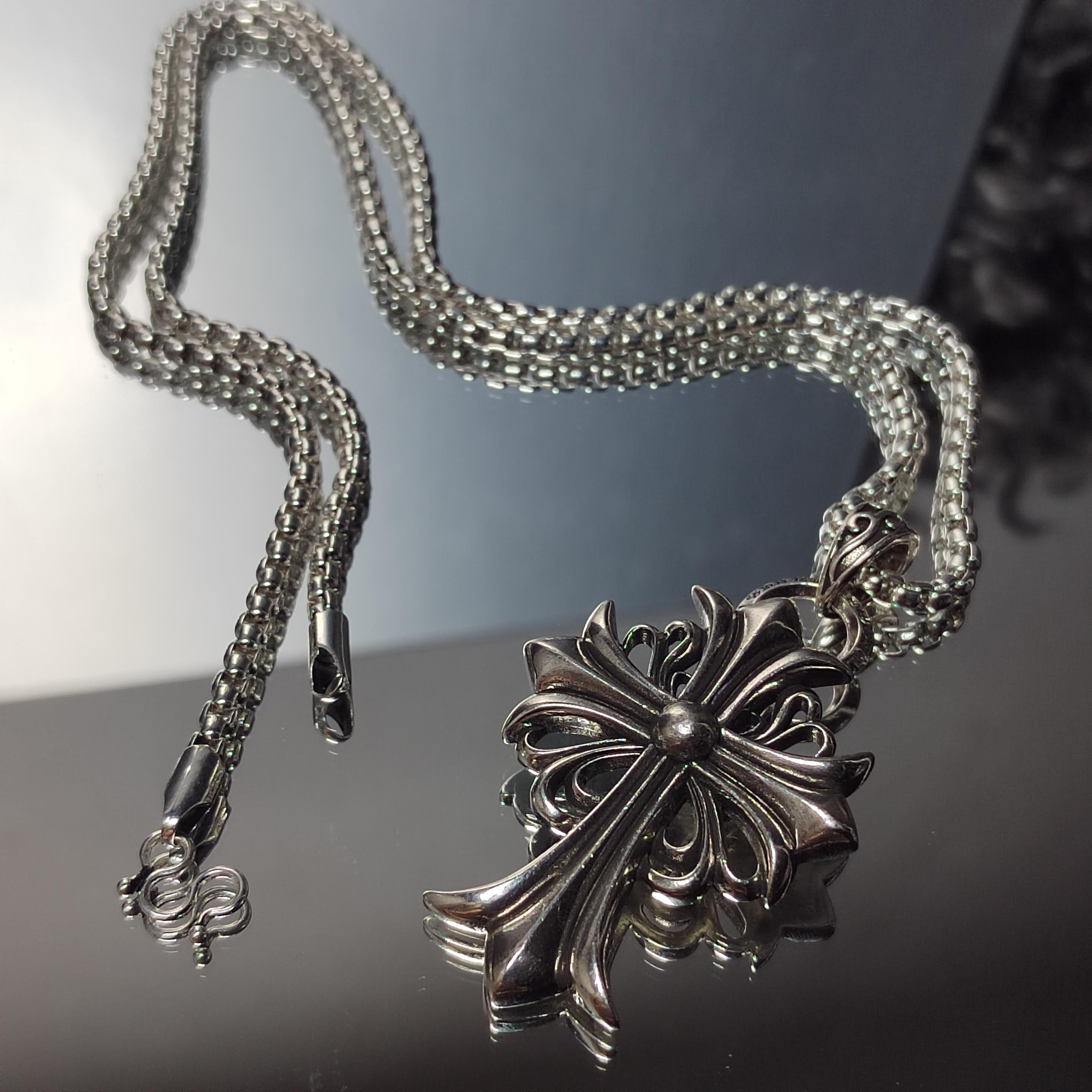 Silver necklace with an intricate pendant on a reflective surface