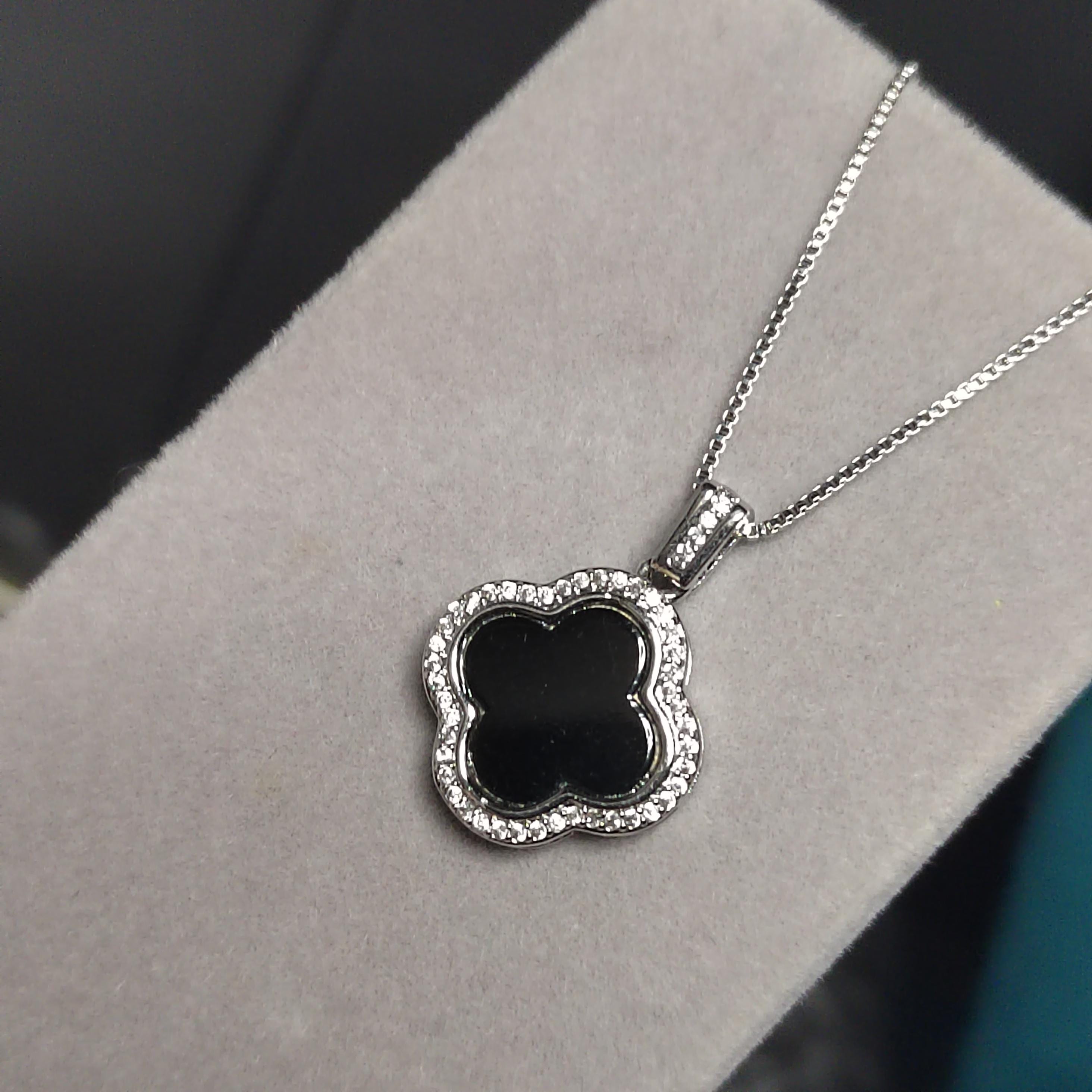 Silver necklace with a black clover pendant on a gray surface